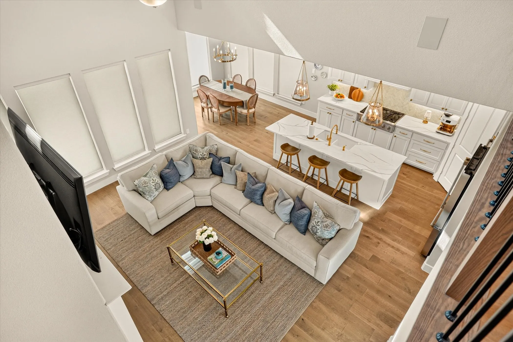 Open-concept living space featuring high ceilings, wood-finish flooring, a kitchen island with seating, white cabinetry, and a dining area with chandelier lighting
