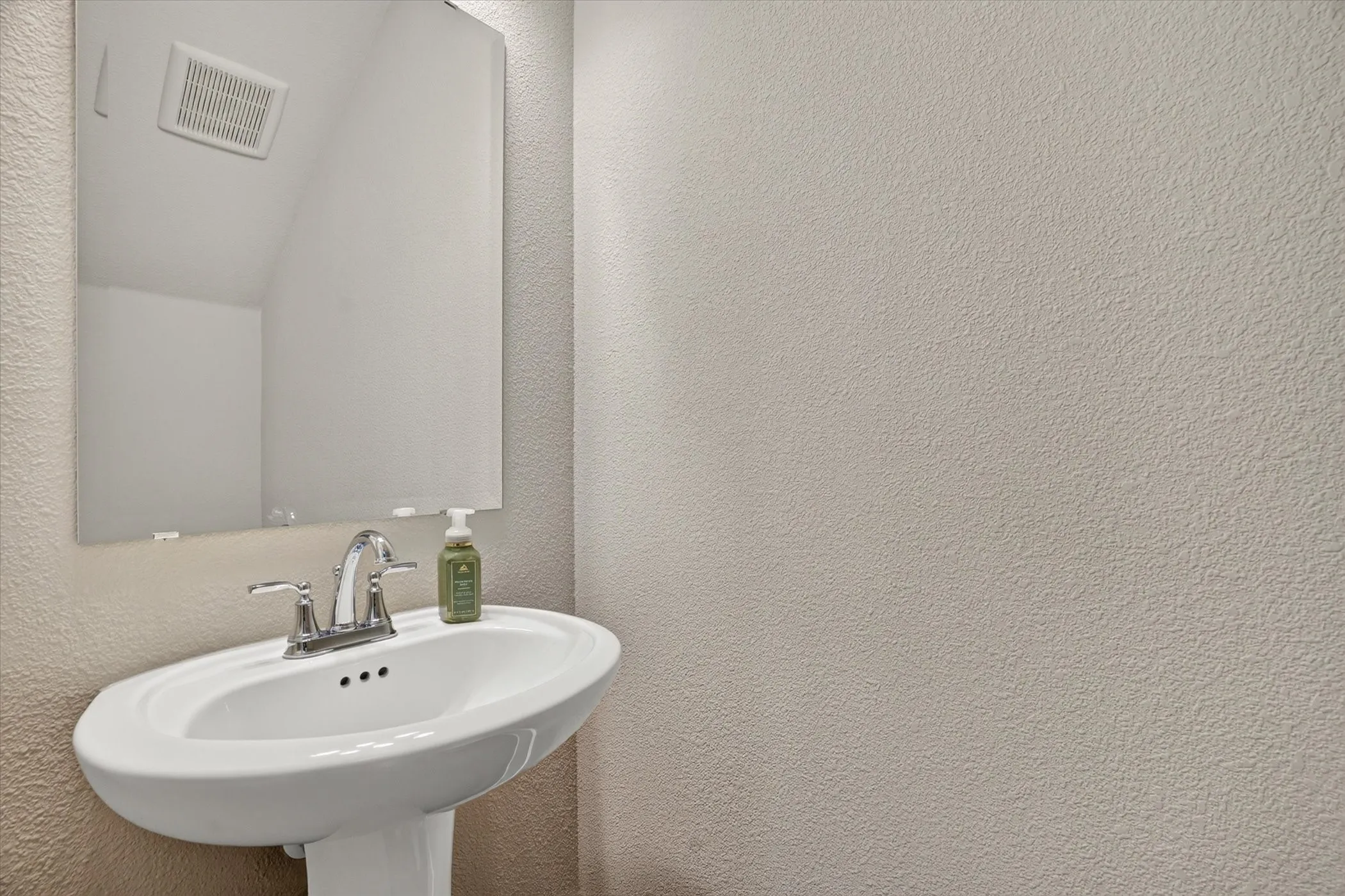 Pedestal sink with chrome faucet hardware and a frameless wall-mounted mirror