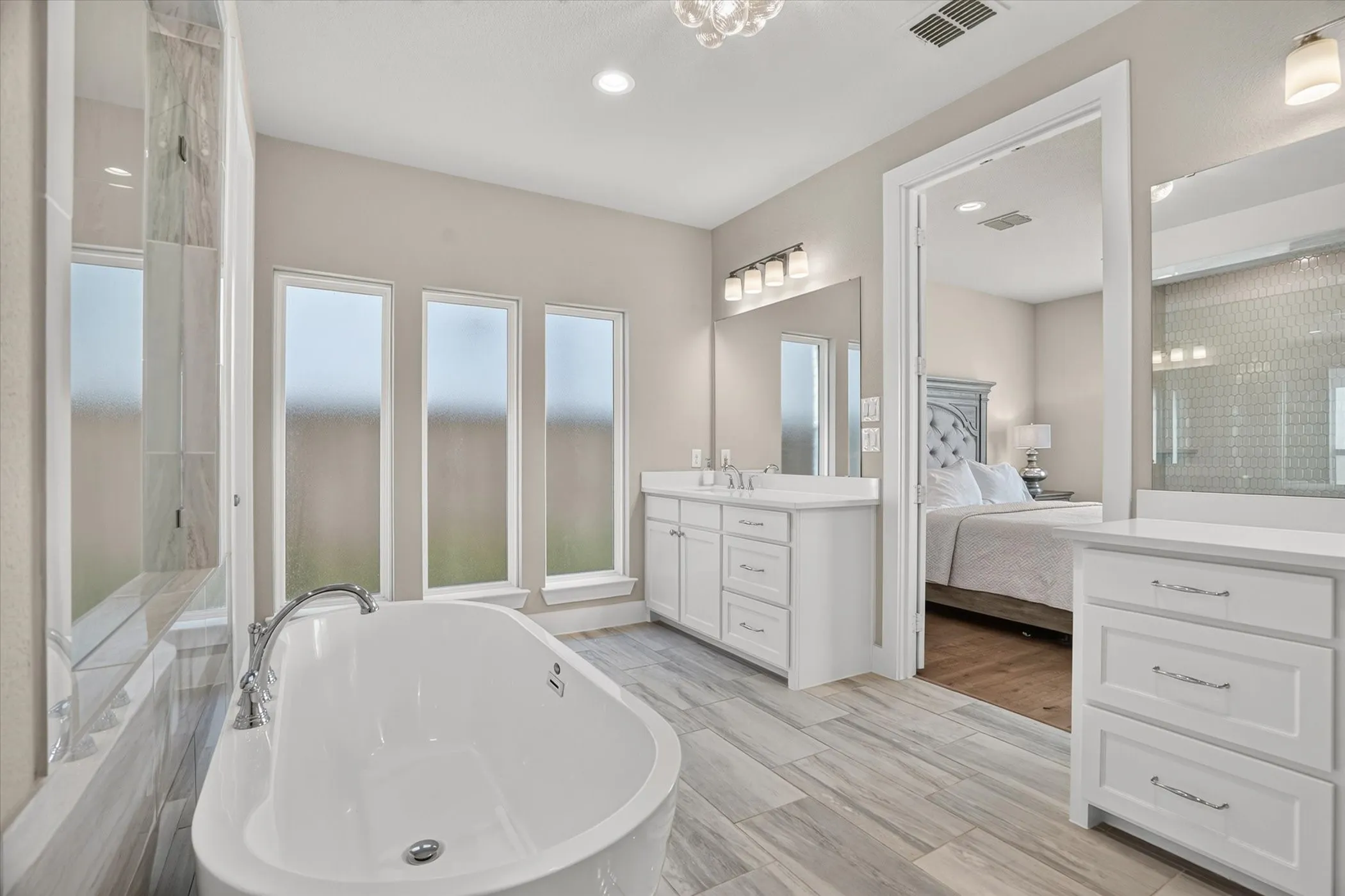 Freestanding soaking tub with chrome fixtures, three vertical privacy windows, and wood-finish flooring