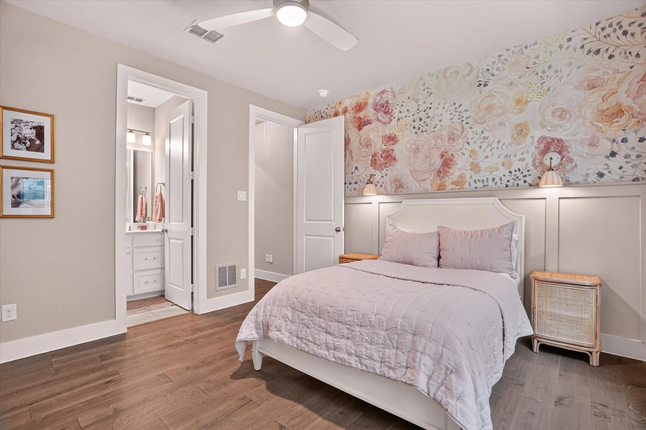 Hardwood-finish flooring extending into a bedroom featuring a decorative floral accent wall with wainscoting and wall-mounted sconces