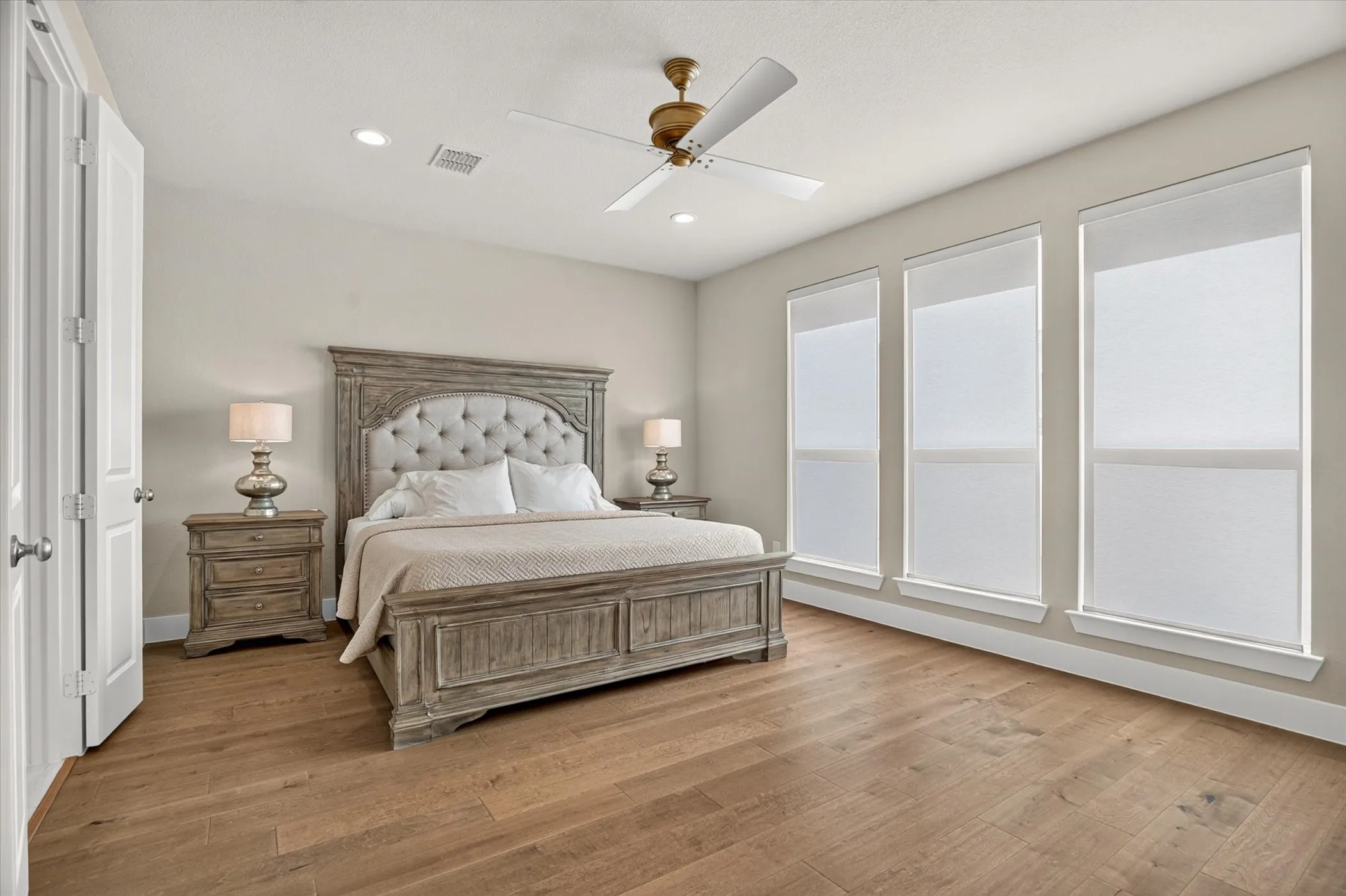 Spacious room featuring wood-finish flooring, three vertical windows with roller shades, and a ceiling fan with integrated lighting