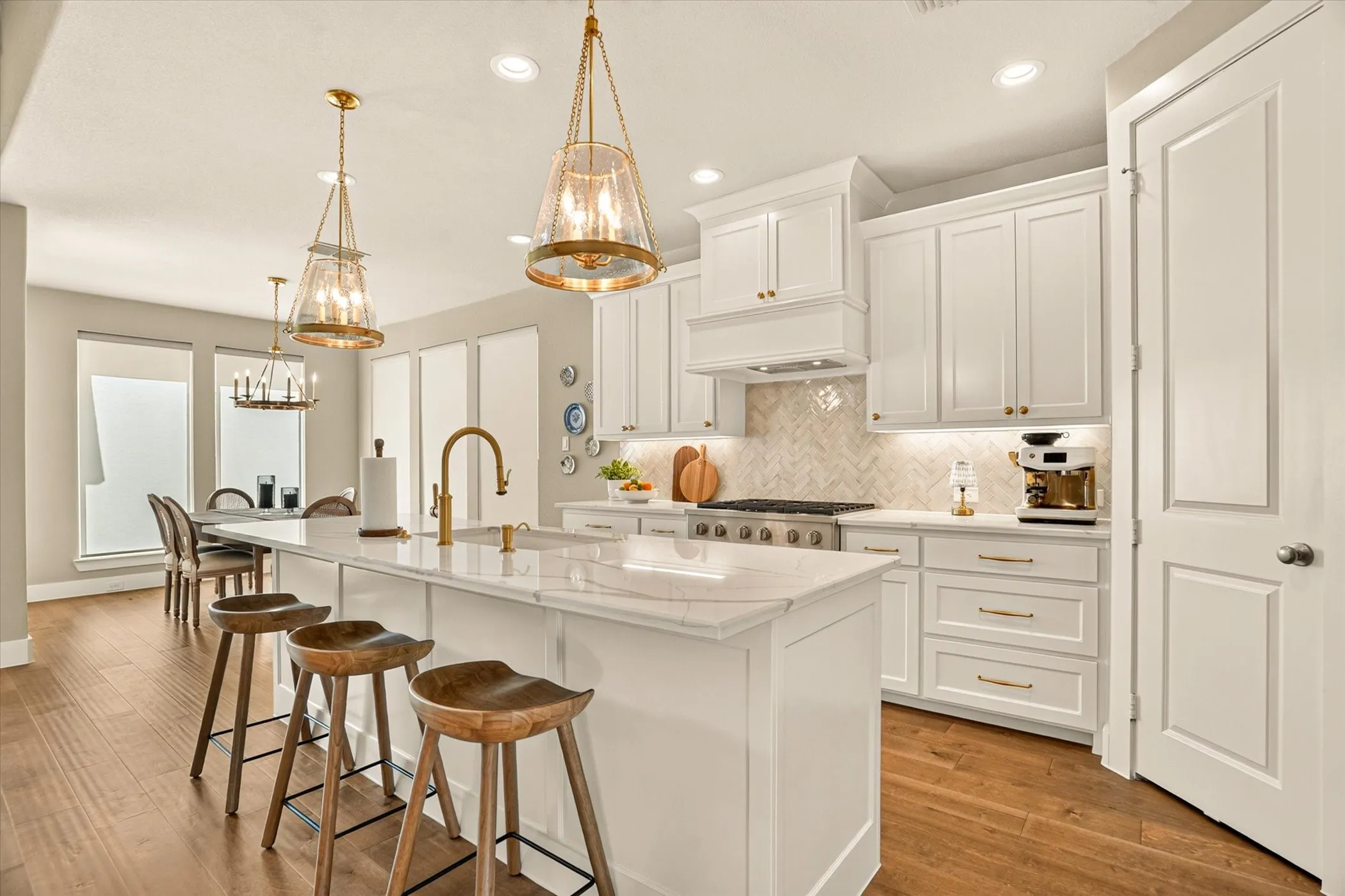 Open-concept kitchen featuring an oversized island with countertop seating, white shaker cabinetry, gold-finish hardware, and wood-finish flooring