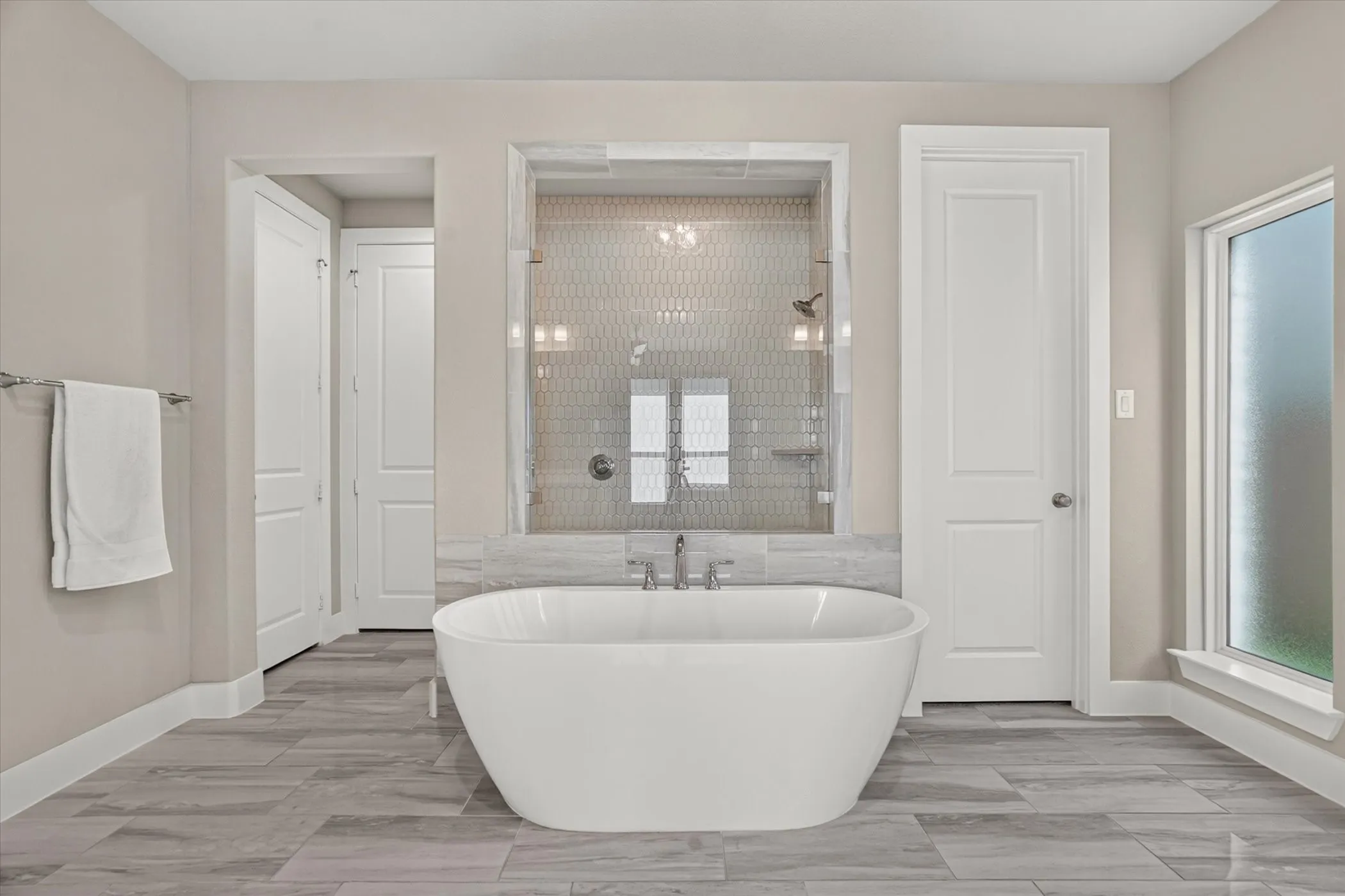 Freestanding soaking tub with a tiled shower enclosure featuring a glass surround, hexagon tile, and dual shower heads