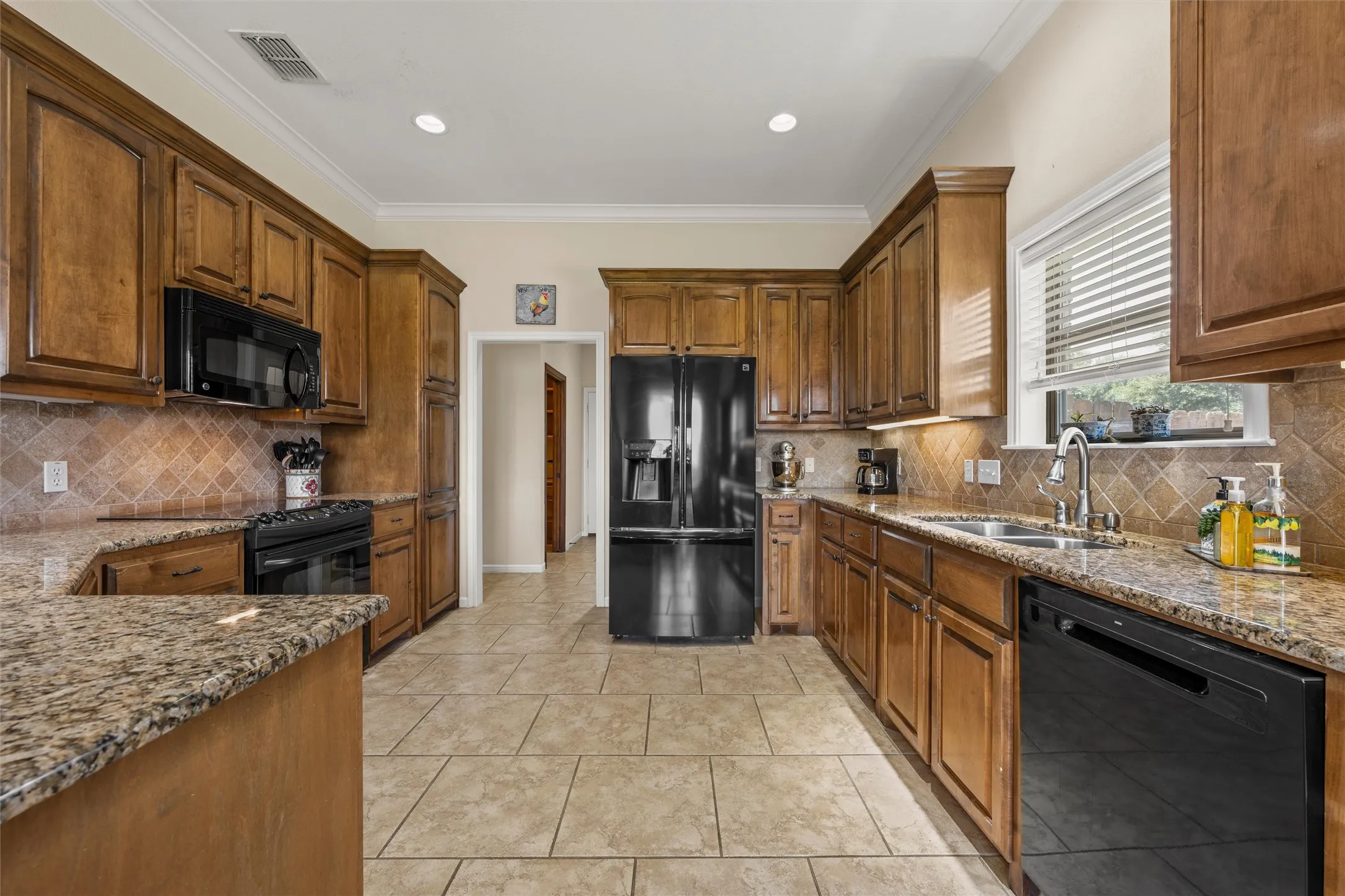 Kitchen featuring extensive wood cabinetry, granite countertops, stainless steel sink, black appliances, and neutral tile flooring