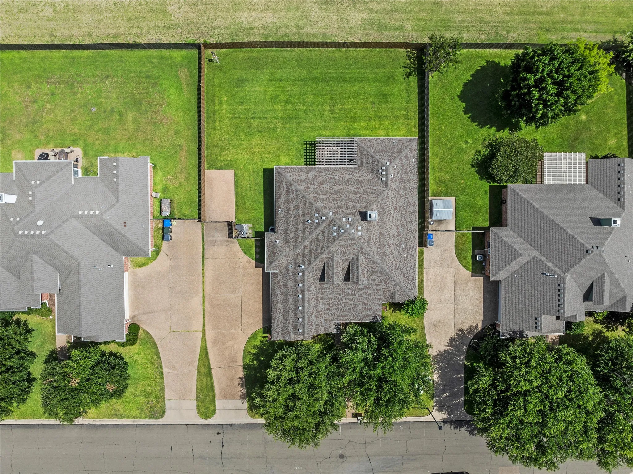 Expansive aerial view showcasing a residential property with a shingled roof and concrete driveway