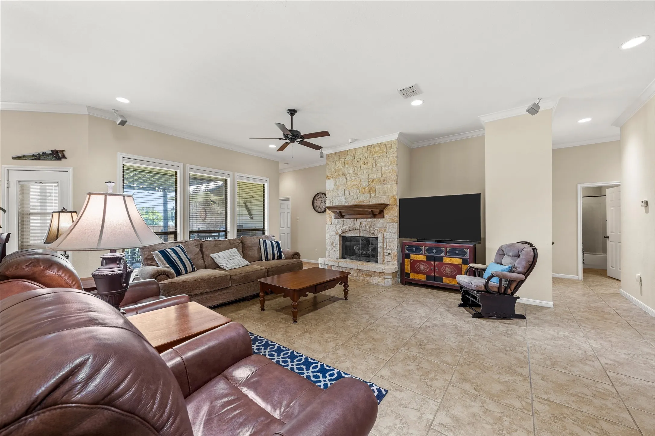 Spacious living area featuring a stone fireplace with a wood mantel, large format tile flooring, crown molding, and recessed lighting