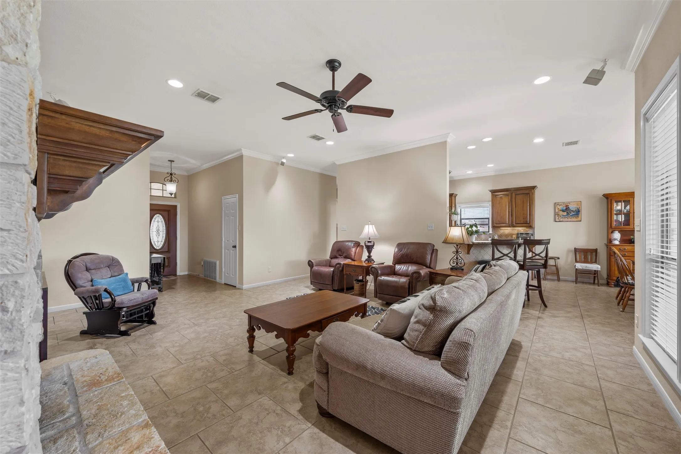 Spacious living area featuring tiled flooring, a stone fireplace surround, and crown molding
