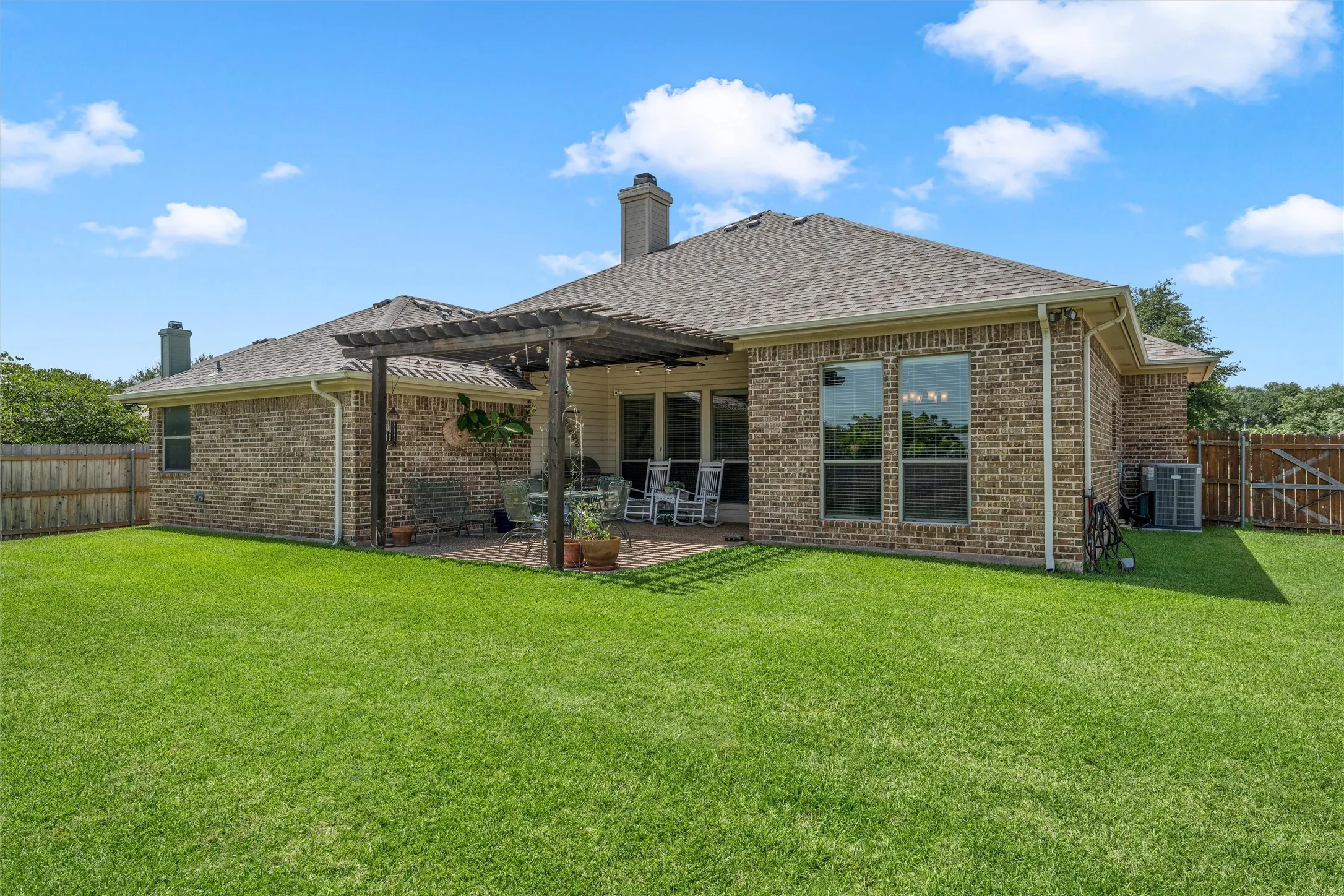 Expansive green lawn bordering a brick exterior with a rear patio featuring a wooden pergola