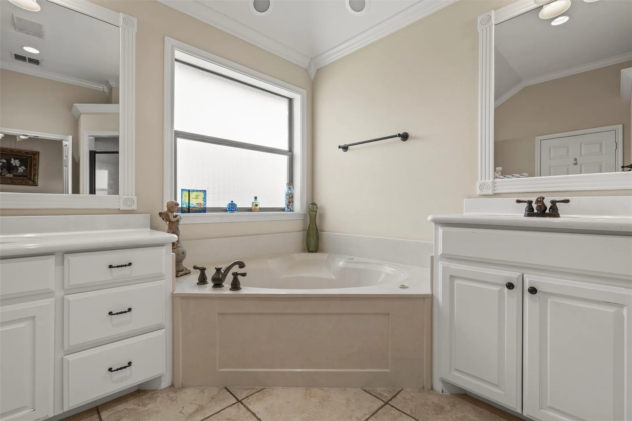 Spacious bathroom featuring a corner soaking tub, dual vanities with white cabinetry, and a large frosted window