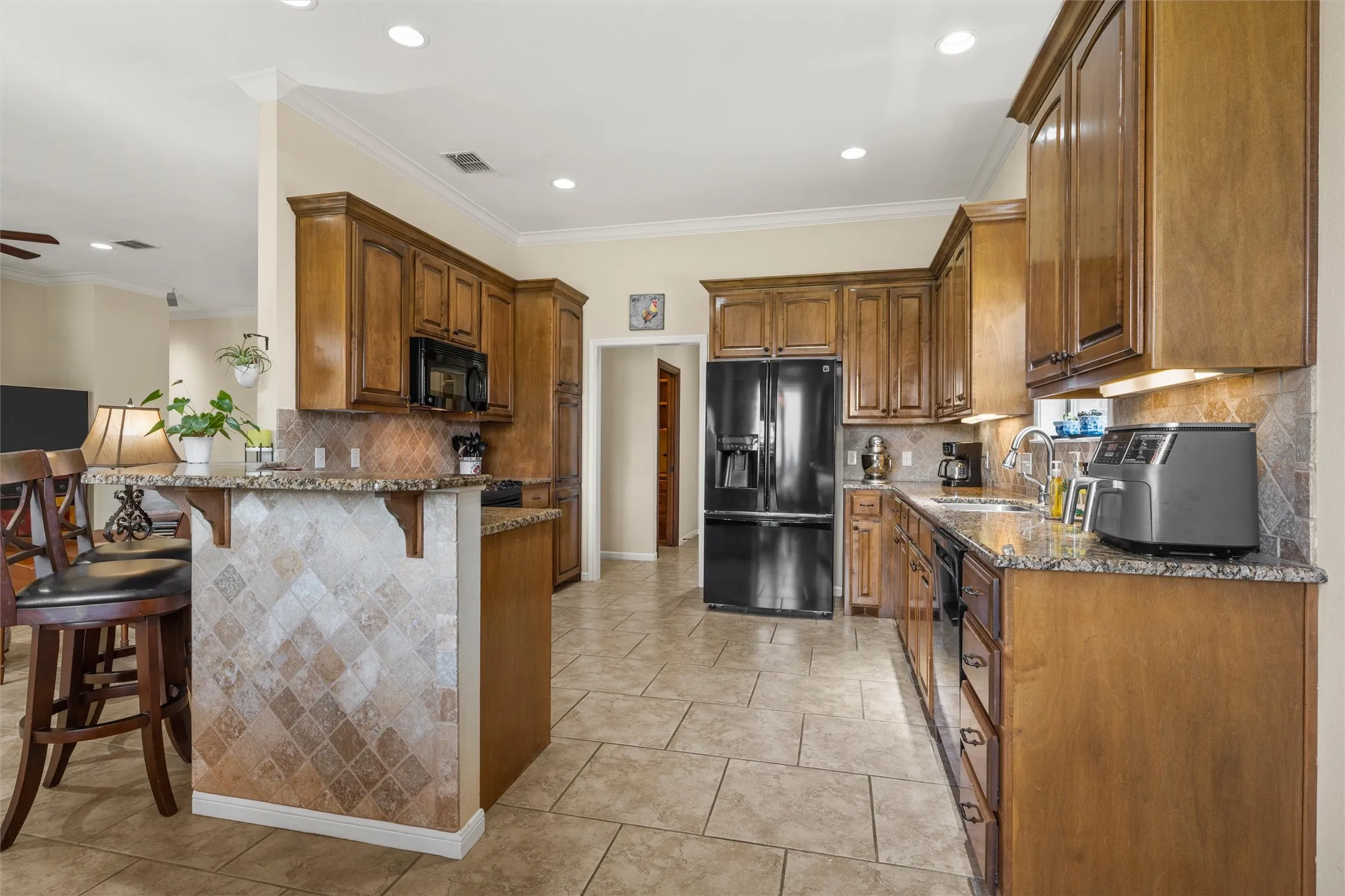 Kitchen featuring wood cabinetry, granite-style countertops, tile flooring, and a breakfast bar with decorative tile accents
