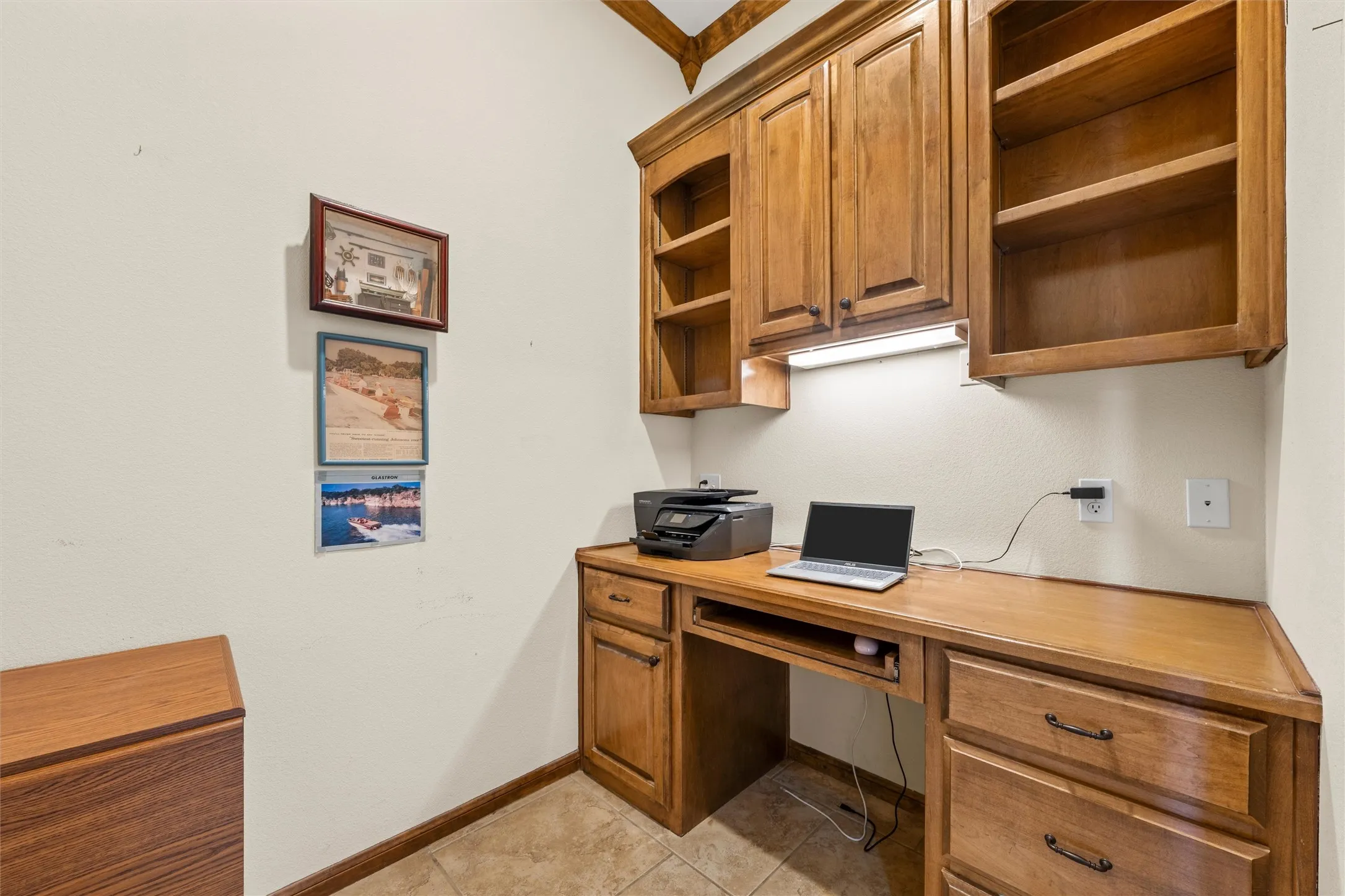 Built-in desk area featuring wood-finish cabinetry, integrated shelving, under-cabinet lighting, and tile flooring