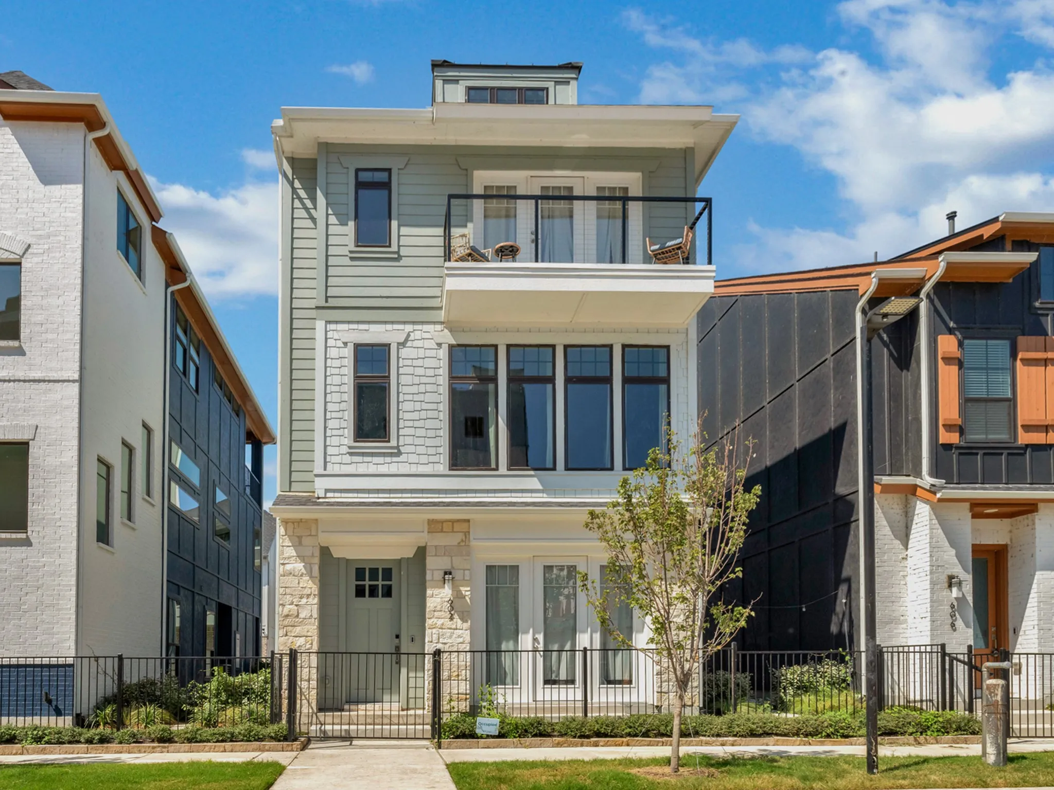 Multi-level residence featuring a stone and siding facade, a glass-paneled entry door, a second-story balcony with a black railing, and a ground-level patio with French doors