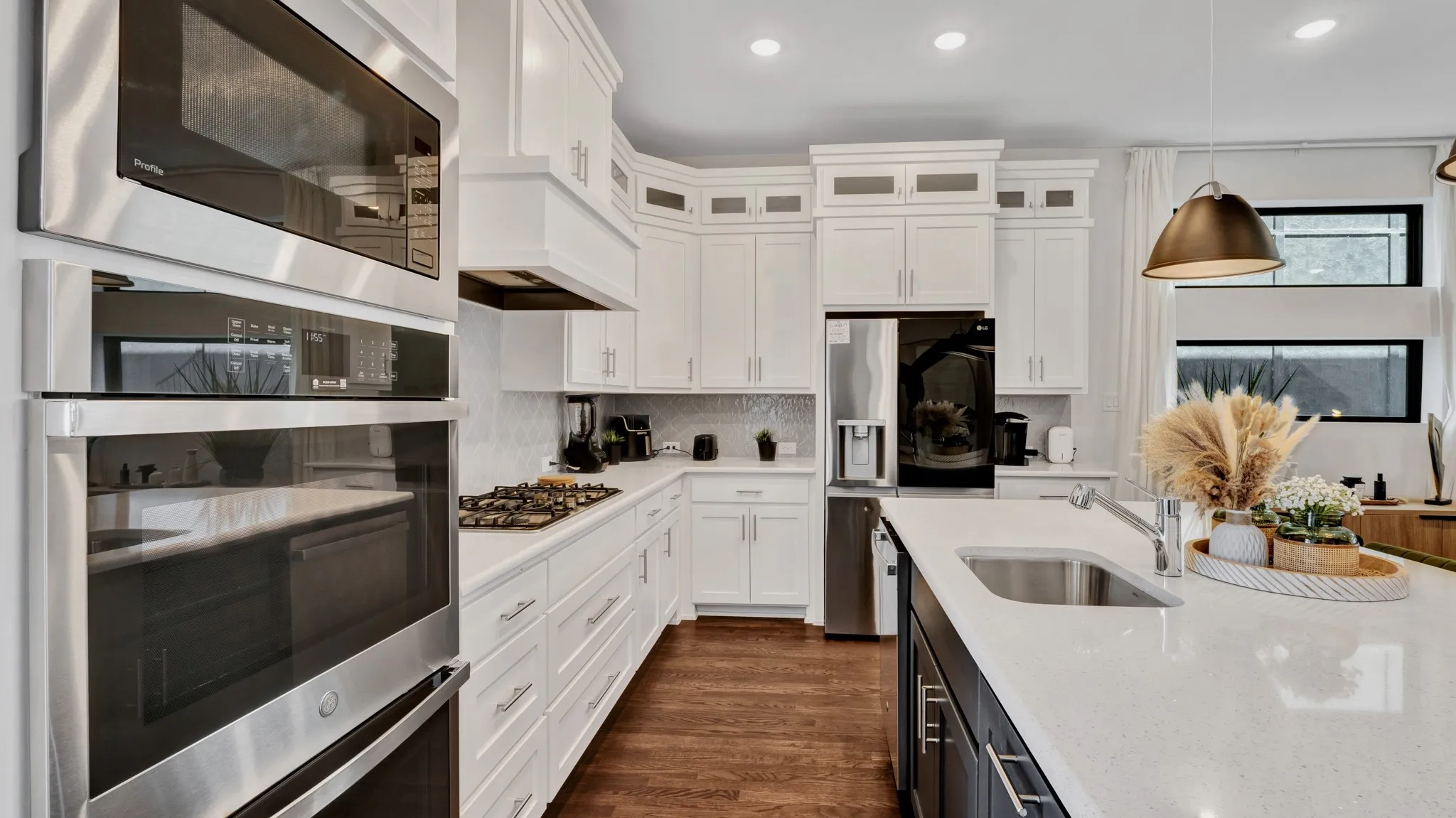 Modern kitchen featuring a gas cooktop, built-in stainless steel appliances, including a doule oven, white cabinetry, wood-finish flooring, and a central island with an undermount sink.