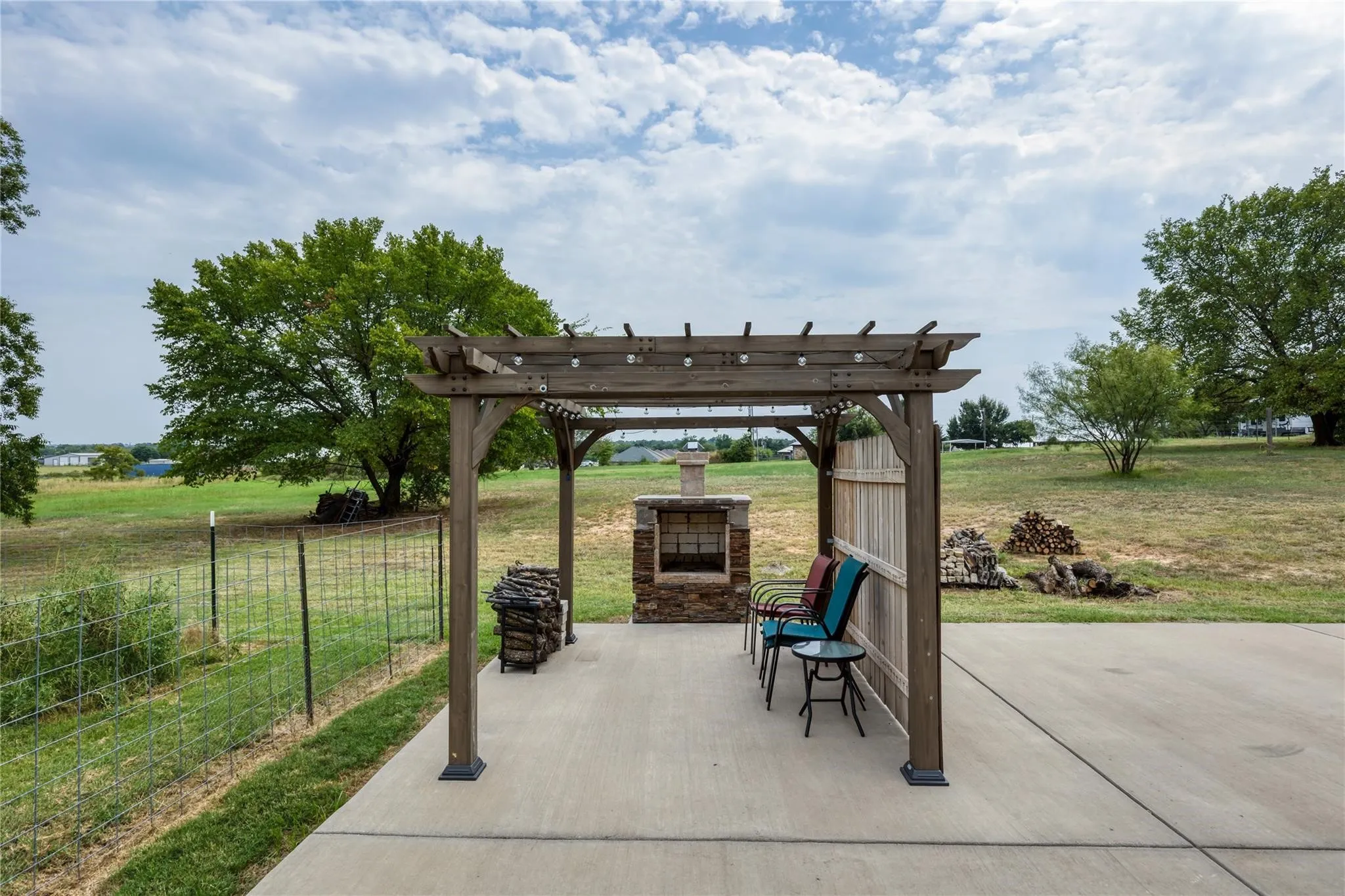 Expansive concrete patio featuring a wood pergola, stone outdoor fireplace, and a partial wood privacy screen