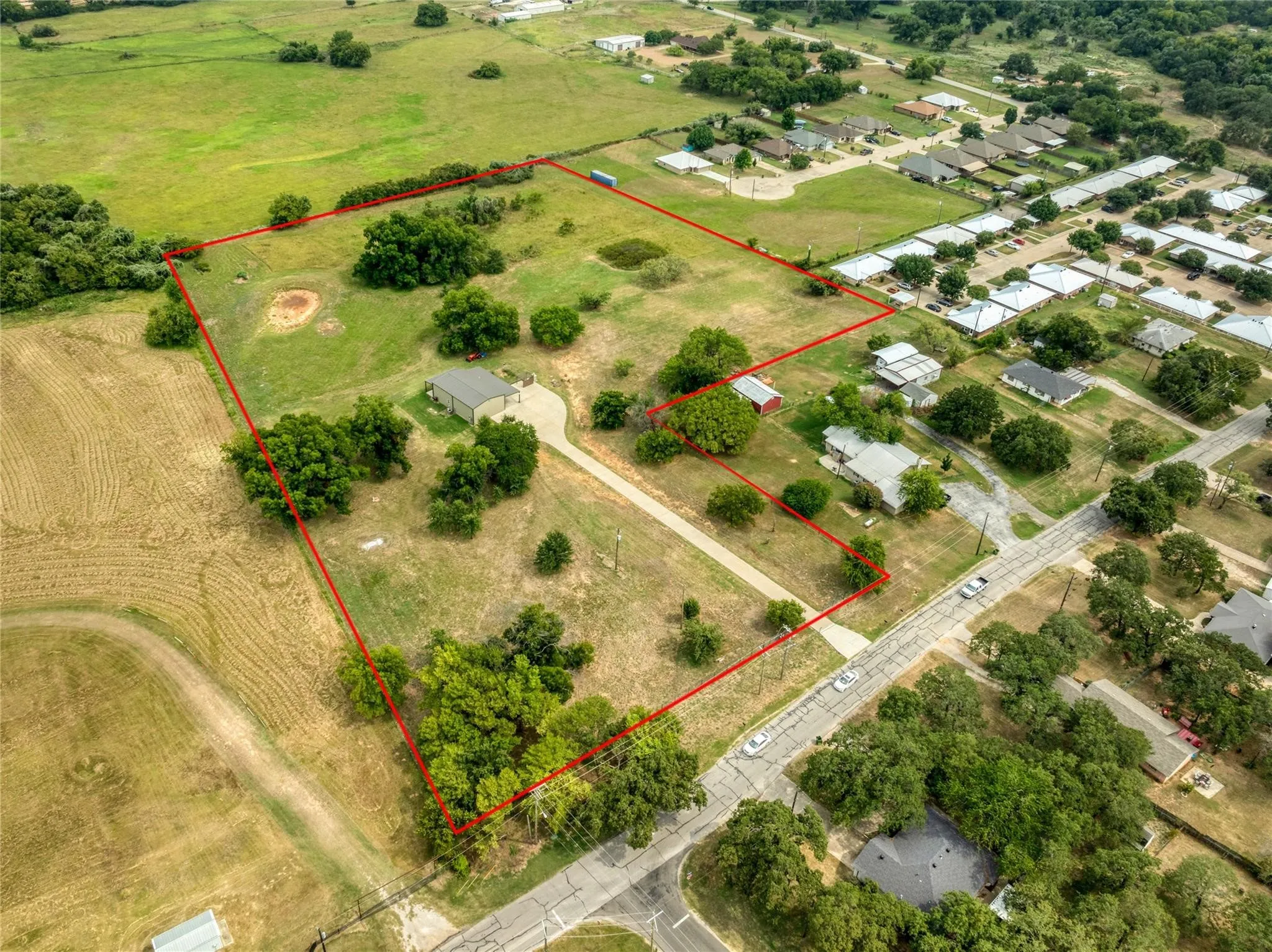 Expansive property featuring a mix of cleared land and mature trees, with a visible concrete driveway