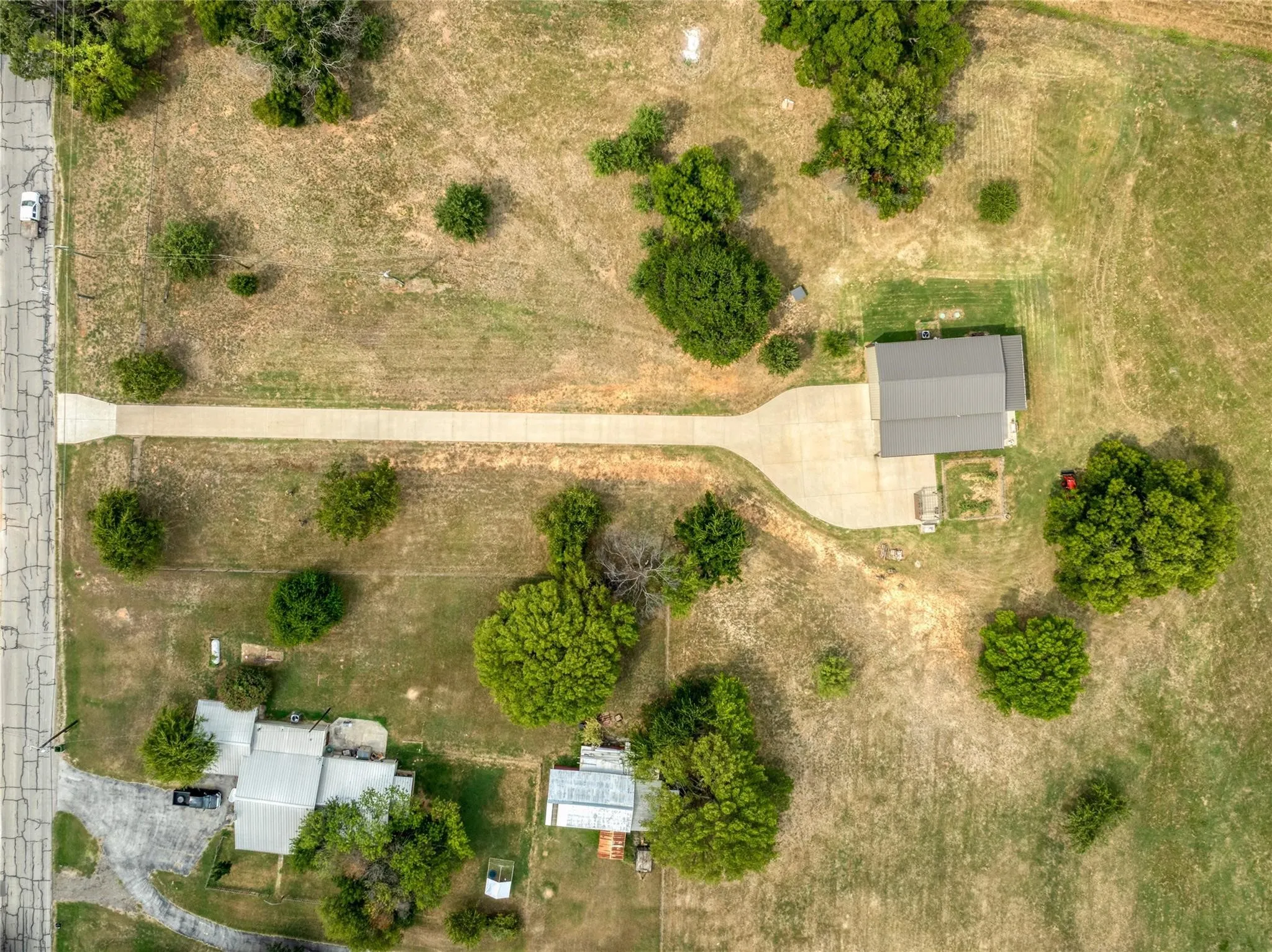 Expansive property featuring two distinct structures, a concrete driveway, and mature landscaping