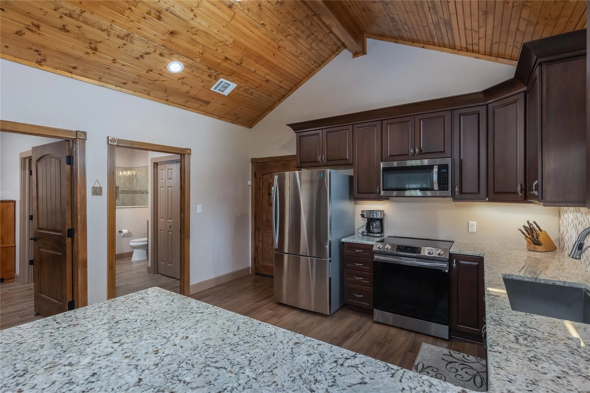 Kitchen featuring wood-finish flooring, vaulted wood plank ceiling, dark wood cabinetry, and stainless steel appliances
