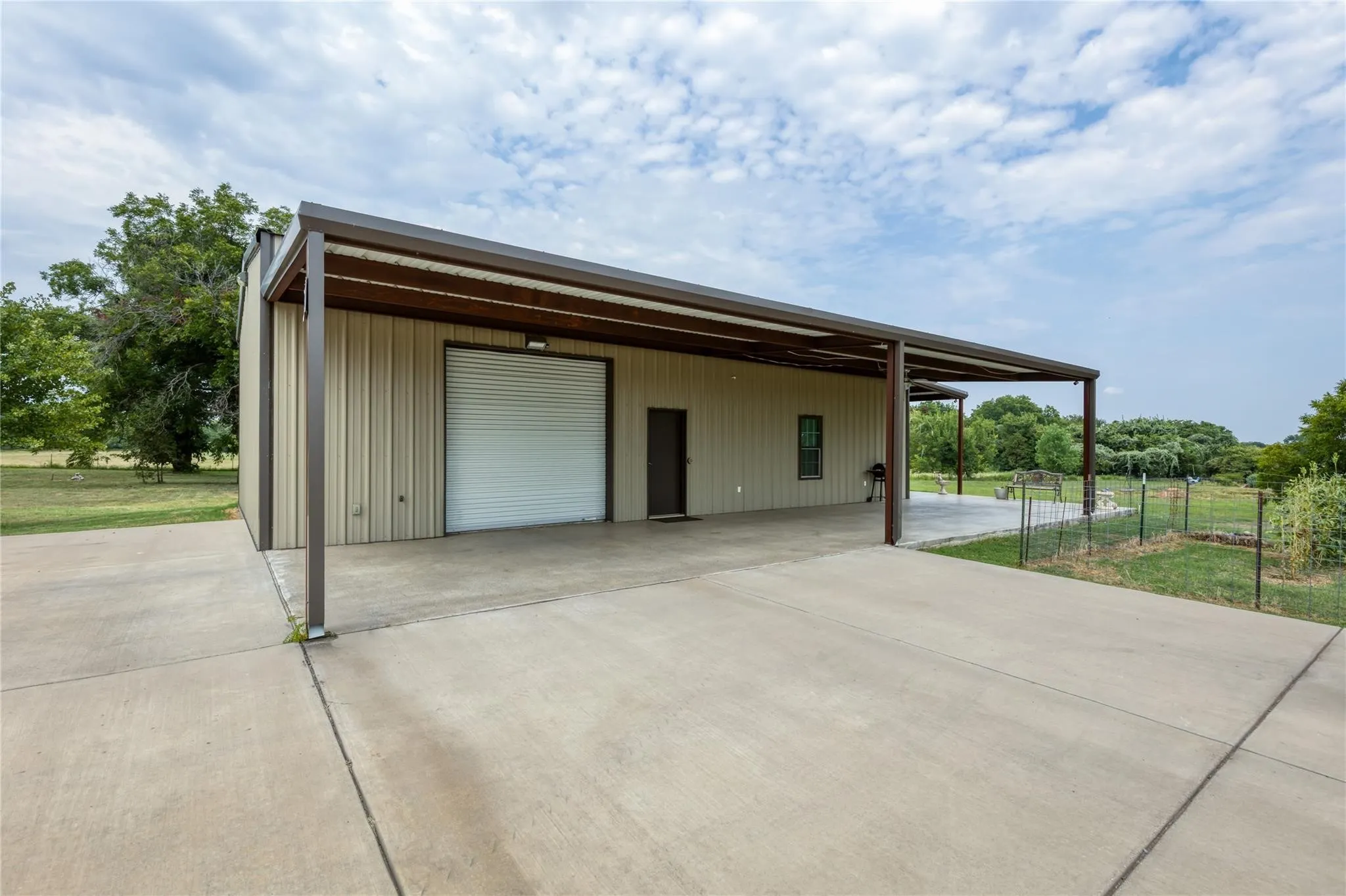 Freestanding structure featuring a large roll-up door, covered carport, and an additional covered patio area