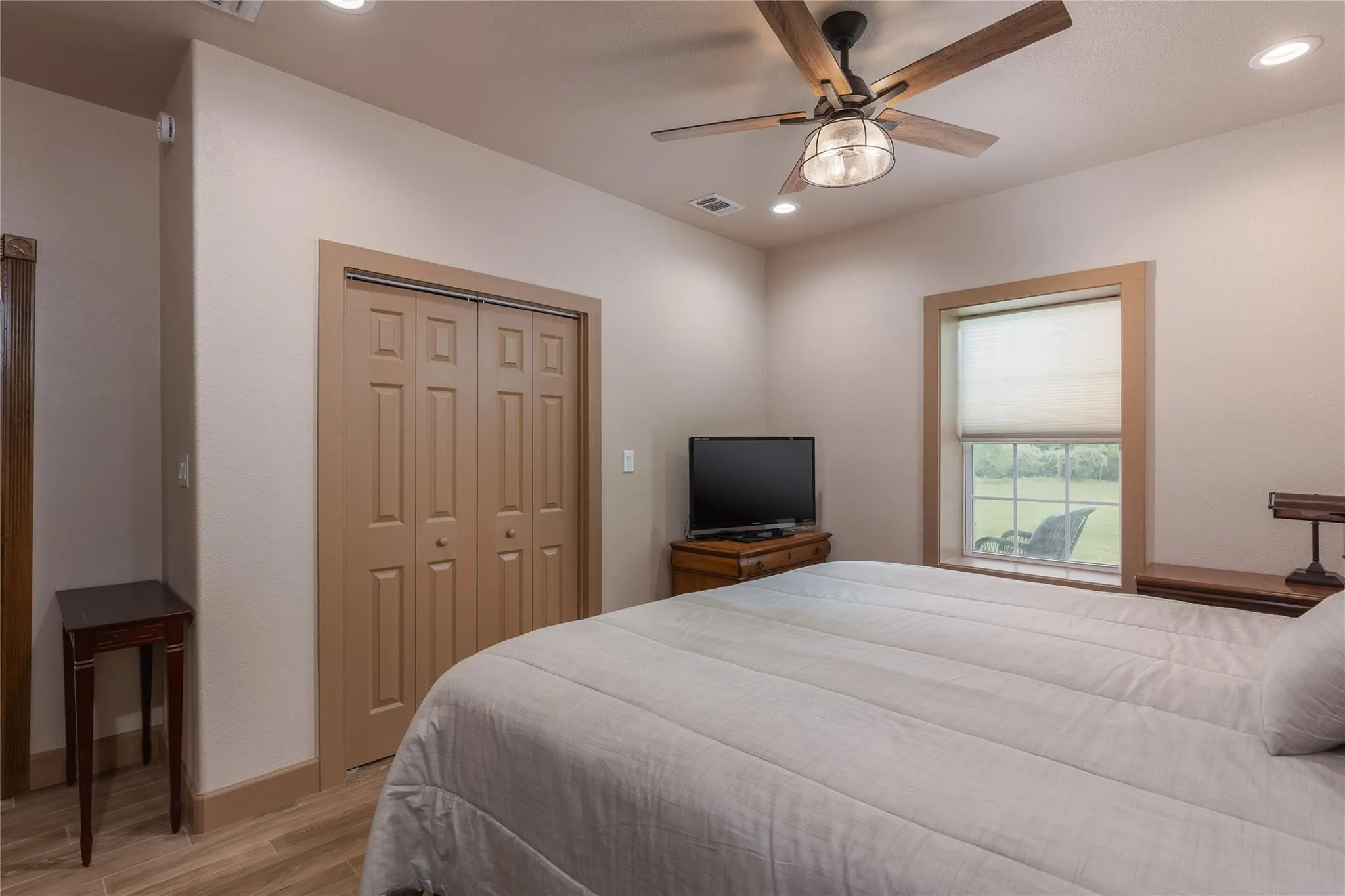 Bedroom featuring a ceiling fan with light fixture, recessed lighting, wood-finish flooring, a window with a roller shade, and bi-fold closet doors