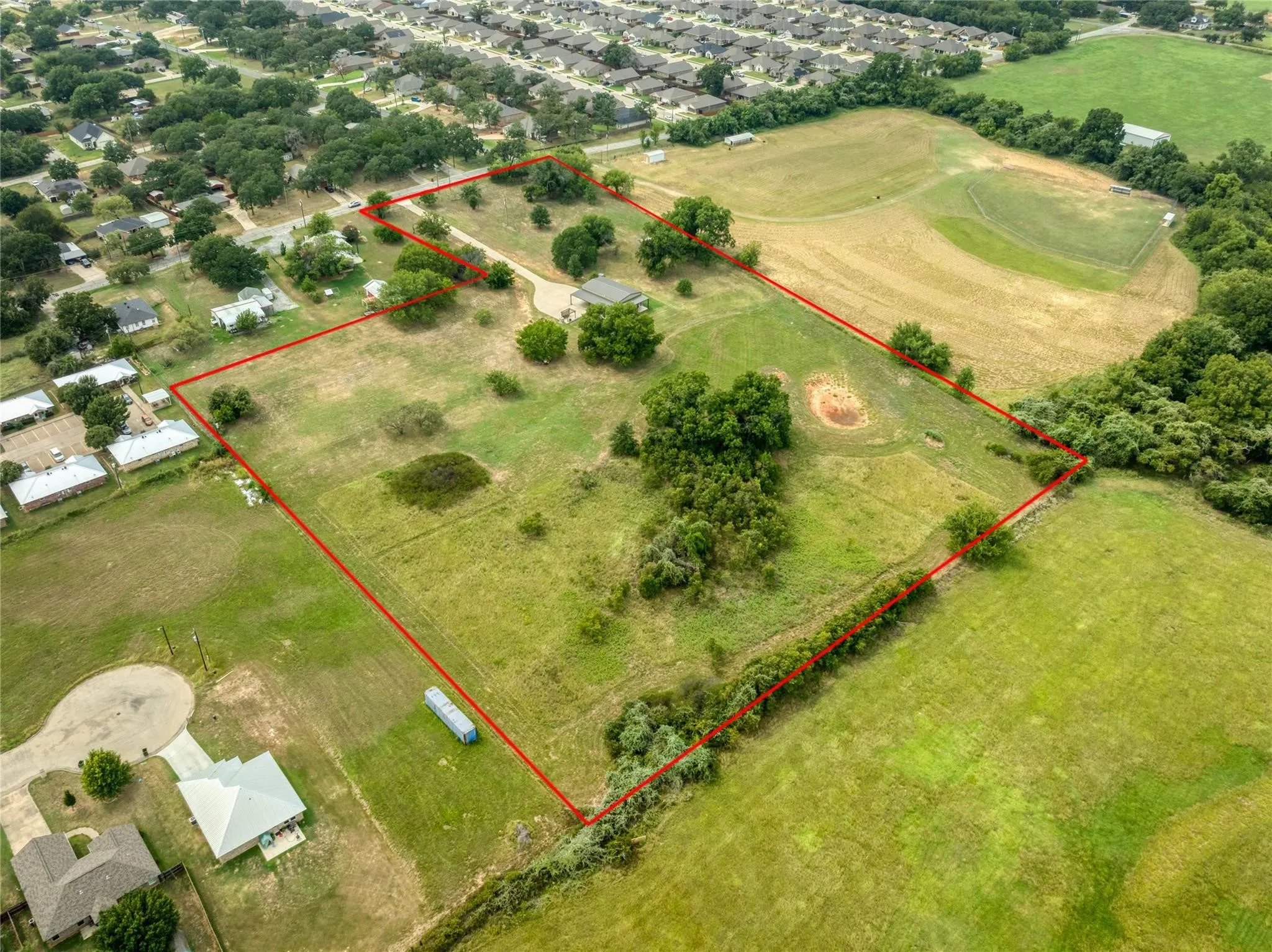 Expansive land parcel featuring a main residence, mature trees, open grassy areas, and a defined boundary line