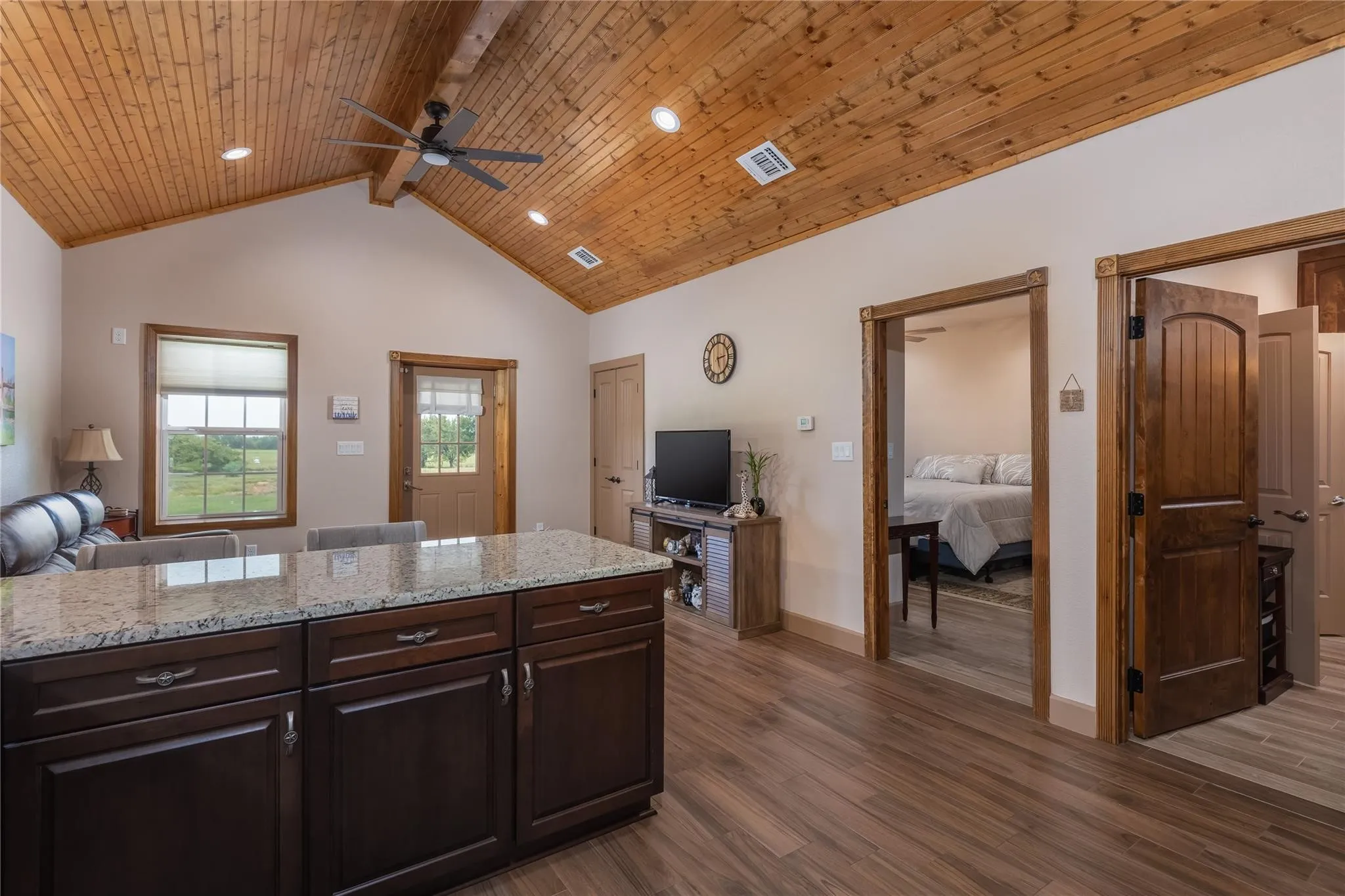 Open-concept living space featuring a granite-topped island with storage, wood-finish flooring, and a vaulted tongue-and-groove wood ceiling with exposed beam accents