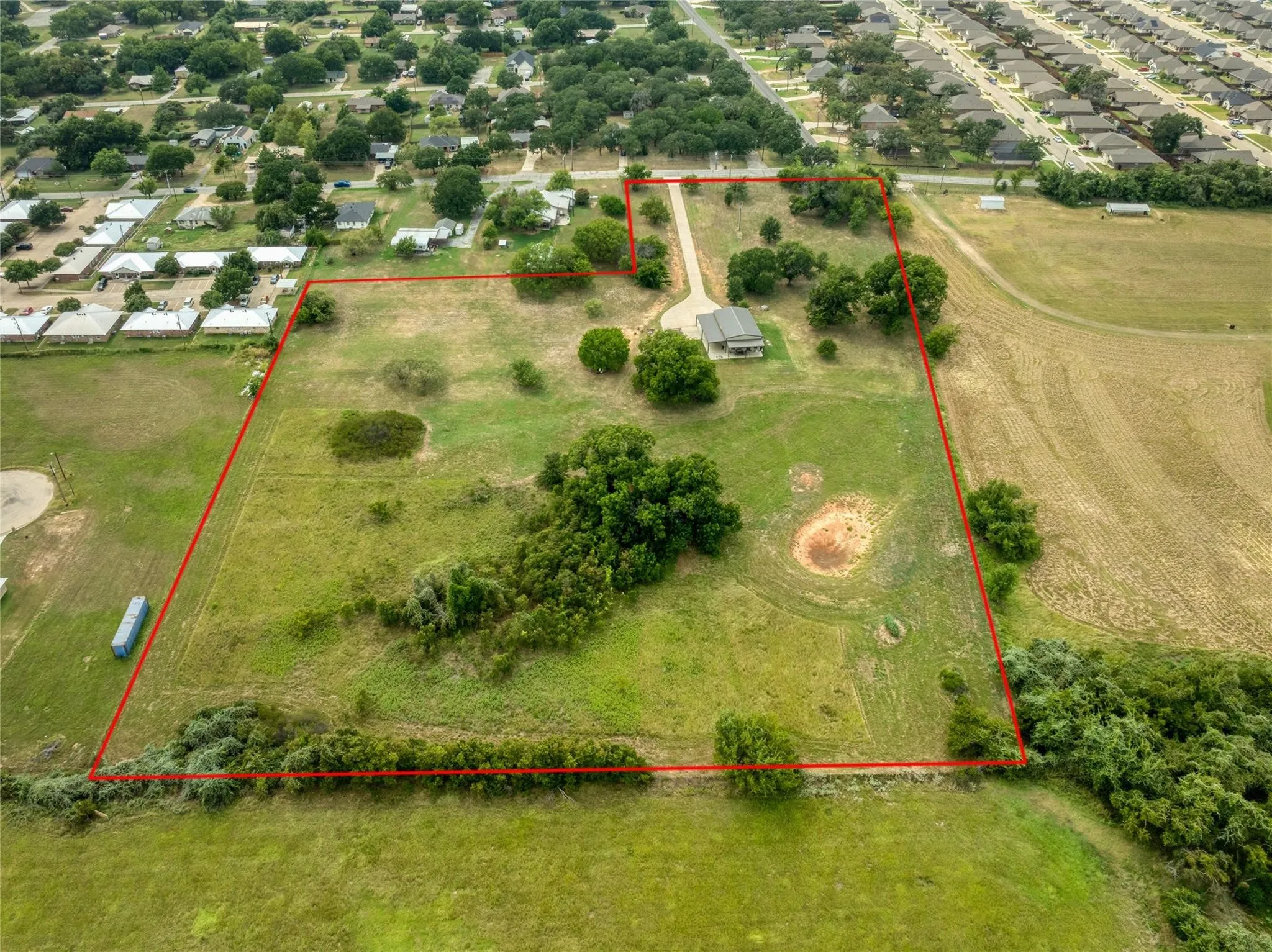 Expansive property featuring a single-story residence, a long private driveway, scattered mature trees, and open land bordered by natural vegetation
