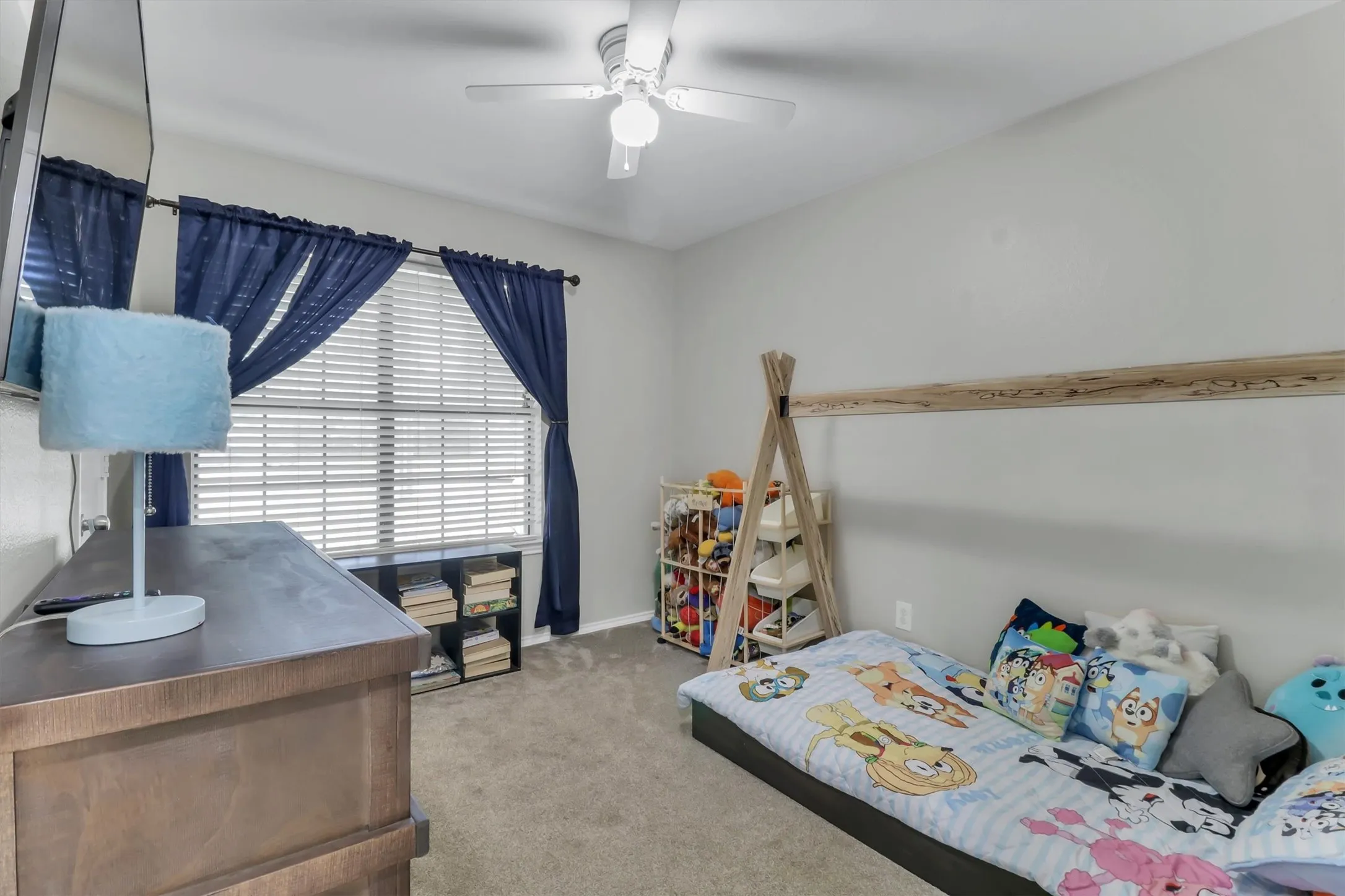 Carpeted room featuring a ceiling fan, a window with horizontal blinds, and a built-in wall shelf