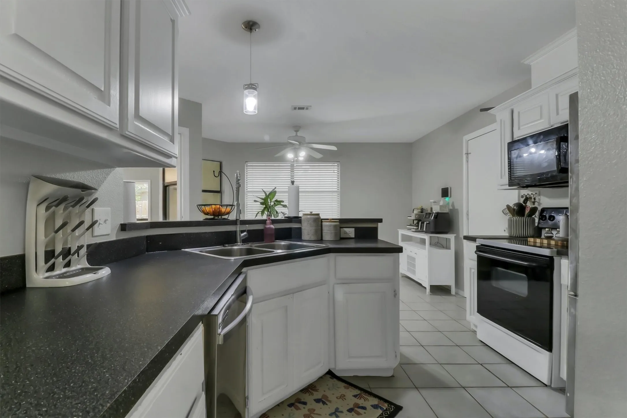 Kitchen featuring white cabinetry, dark speckled countertops, stainless steel double basin sink, tile flooring, and a built-in microwave