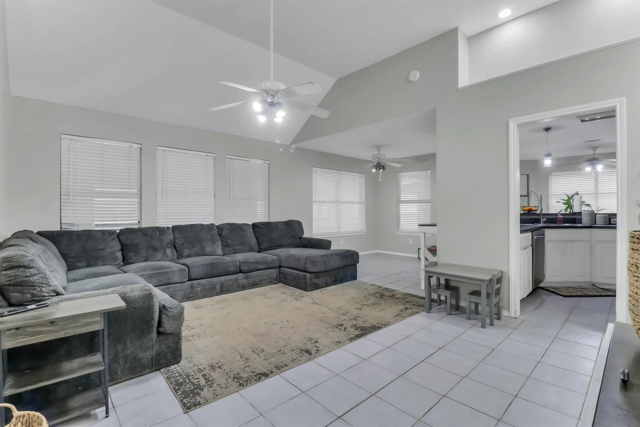 Vaulted ceiling in a spacious living area featuring tiled flooring and multiple windows with blinds