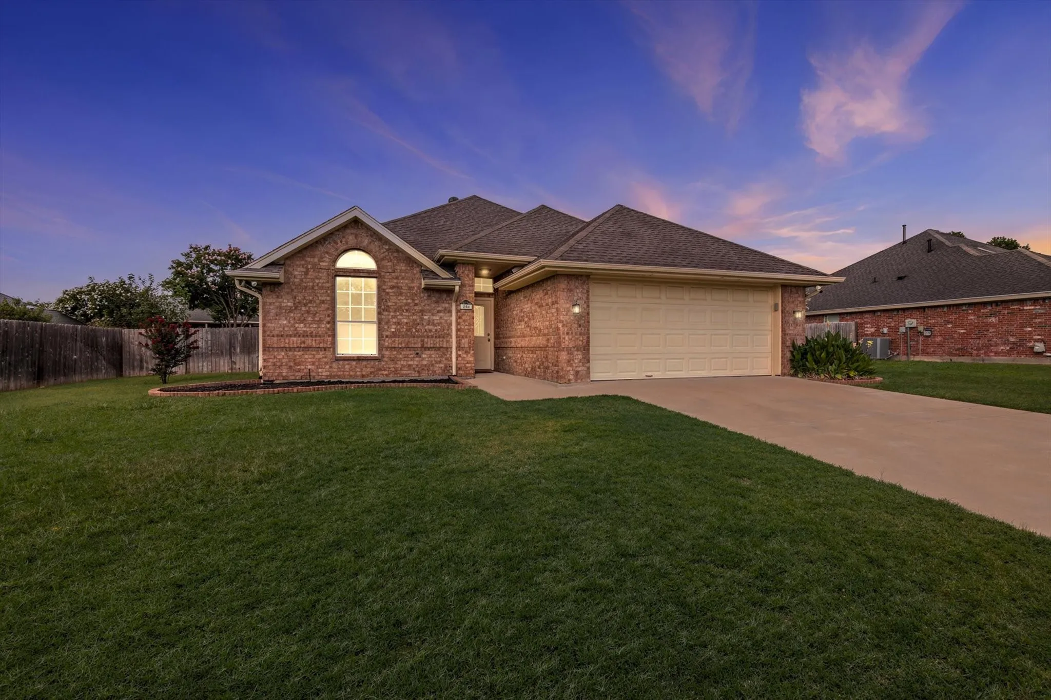 Brick exterior with an arched window accent, attached two-car garage, concrete driveway, and a front lawn