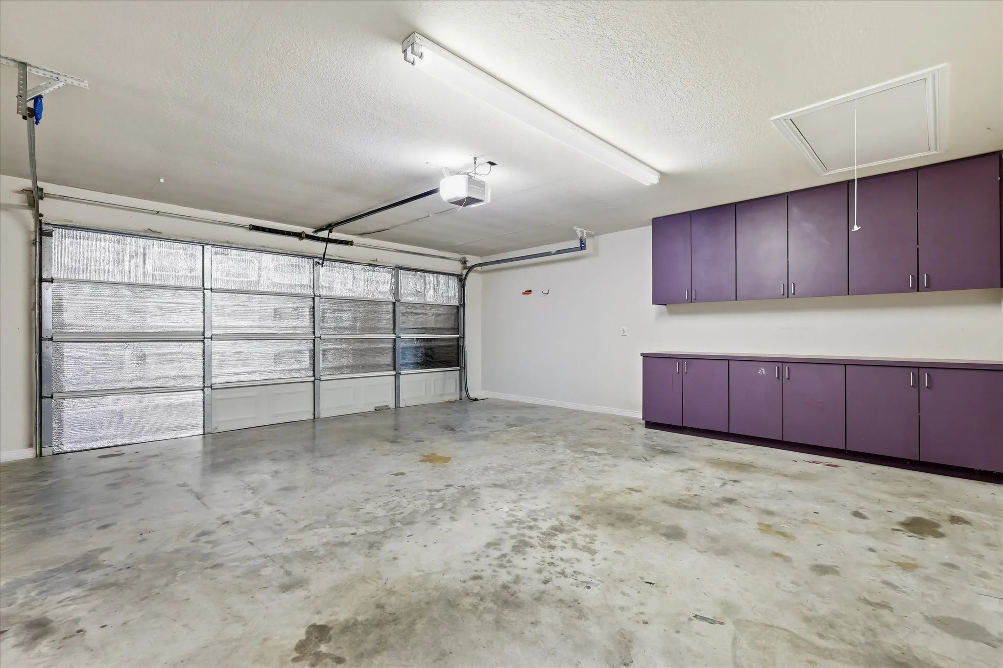 Two-car garage featuring a concrete floor, built-in purple cabinetry, and an attic access panel