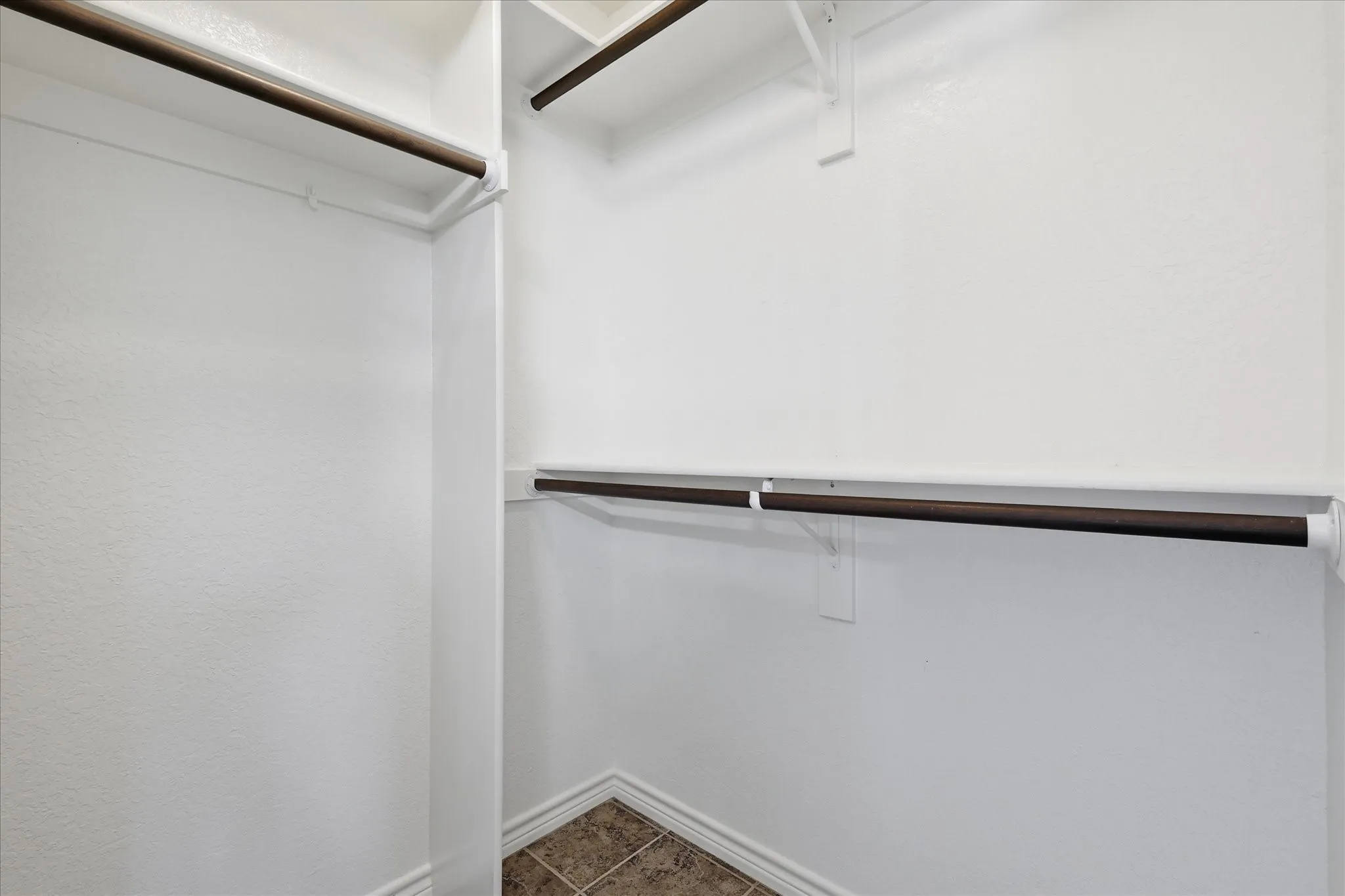 Walk-in closet with multiple hanging rods, overhead shelving, and tile flooring
