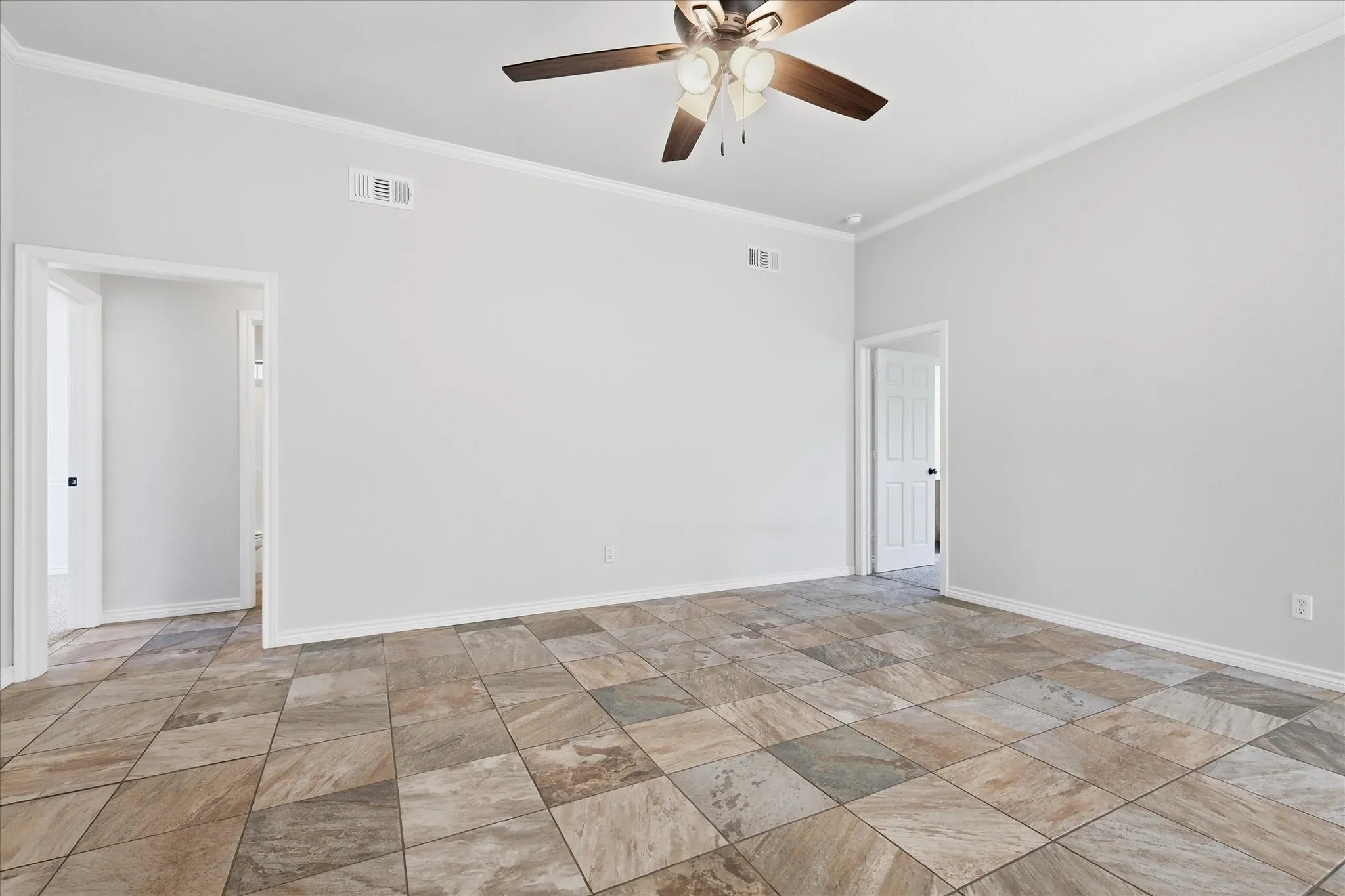 Spacious room featuring variegated tile flooring, crisp white walls, and elegant crown molding