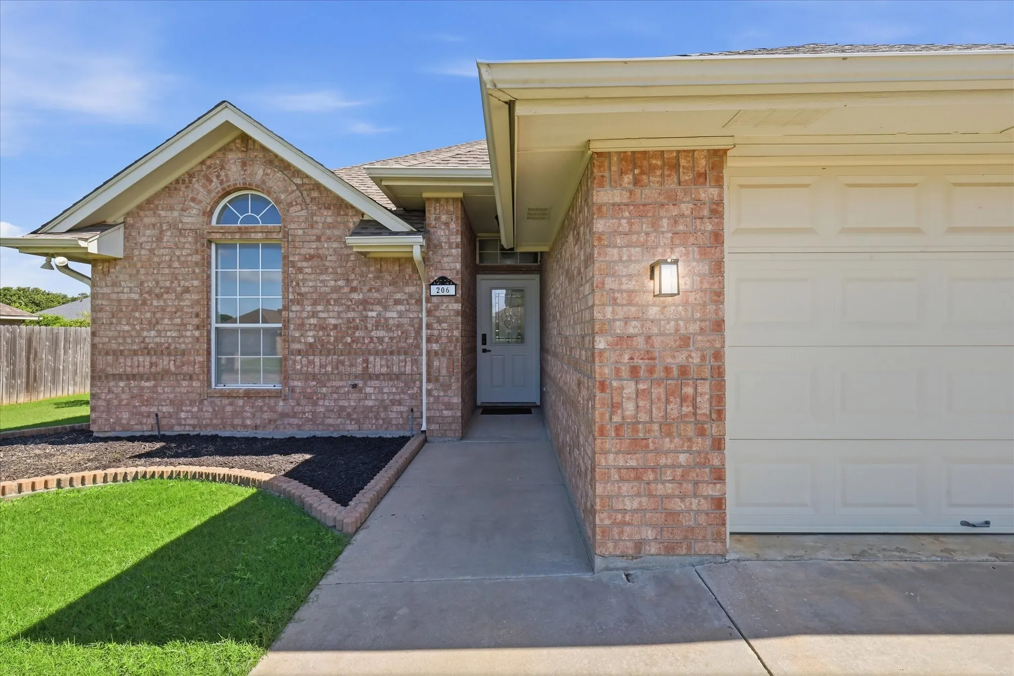 Brick facade home featuring an arched window, attached garage, and concrete walkway