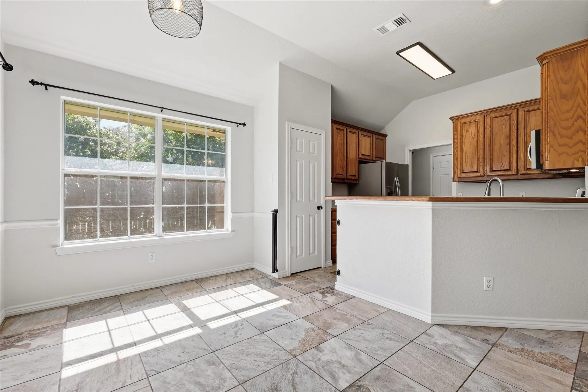 Open-concept living space featuring large windows, neutral-toned tile flooring, and a kitchen peninsula with wood-finish cabinetry