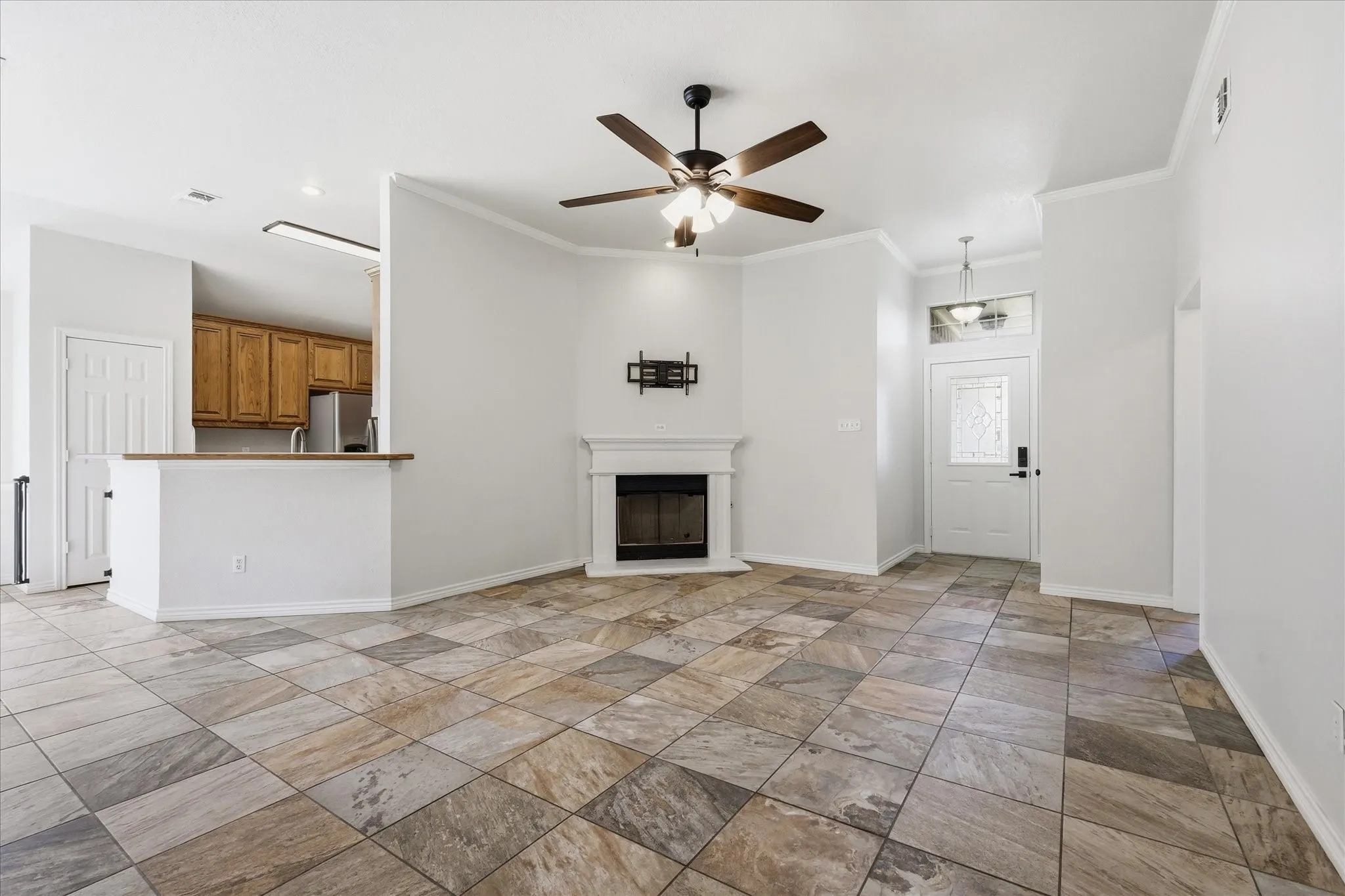 Spacious living area featuring large format tile flooring, a corner fireplace with white mantel, and crown molding