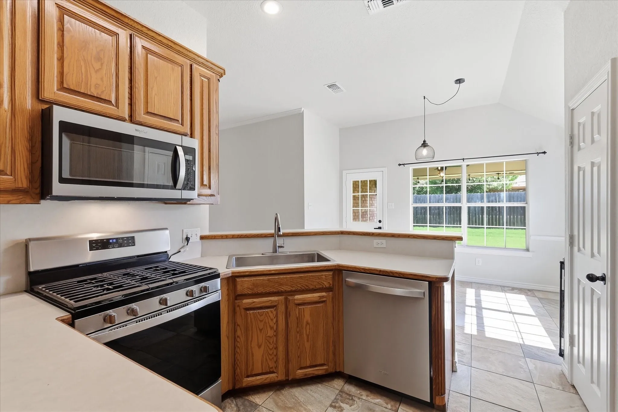 Kitchen featuring wood cabinetry, light-toned countertops, and stainless steel appliances including a gas range, microwave, and dishwasher