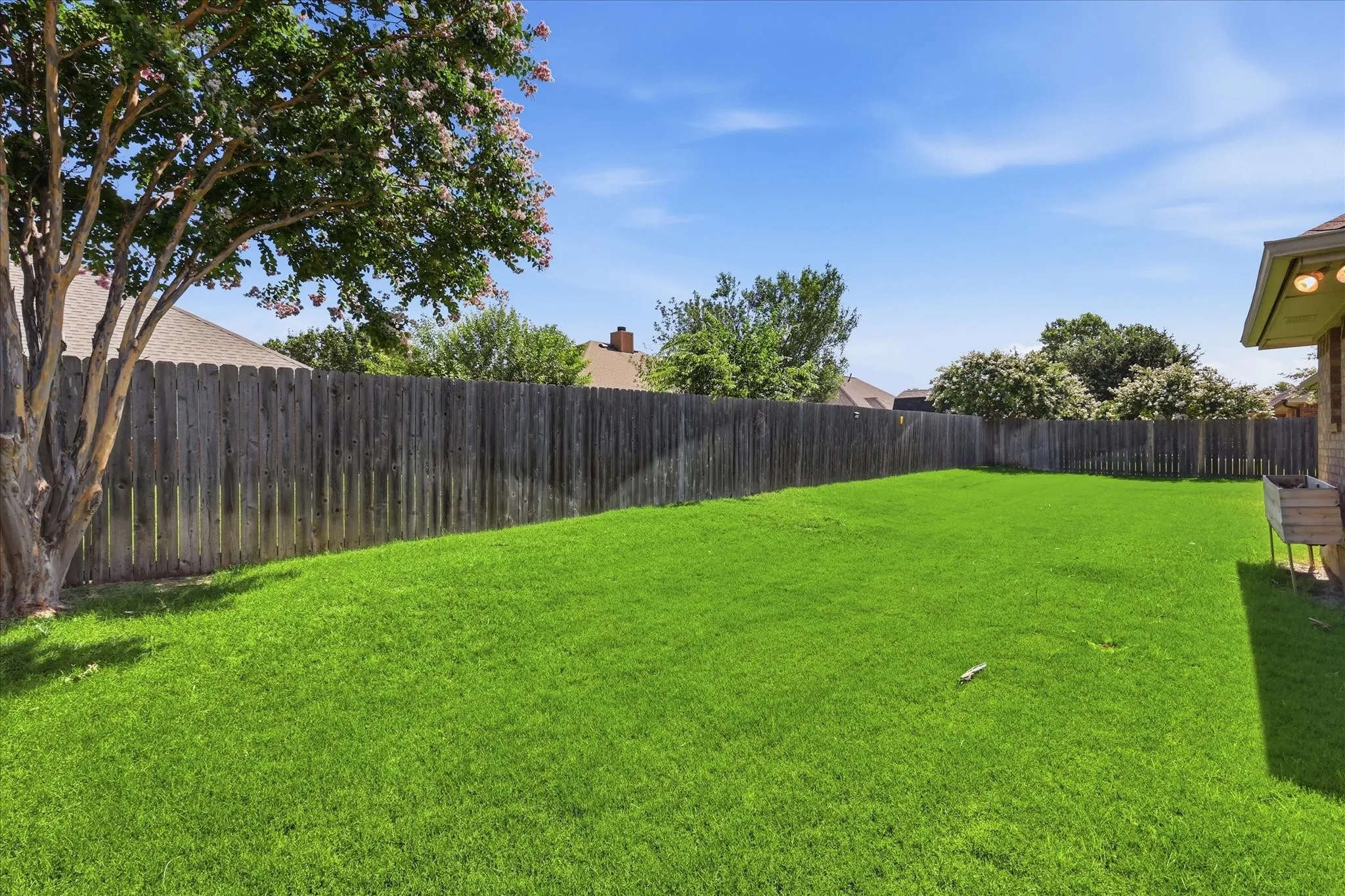 Spacious backyard featuring a lush lawn, privacy fencing, and mature trees