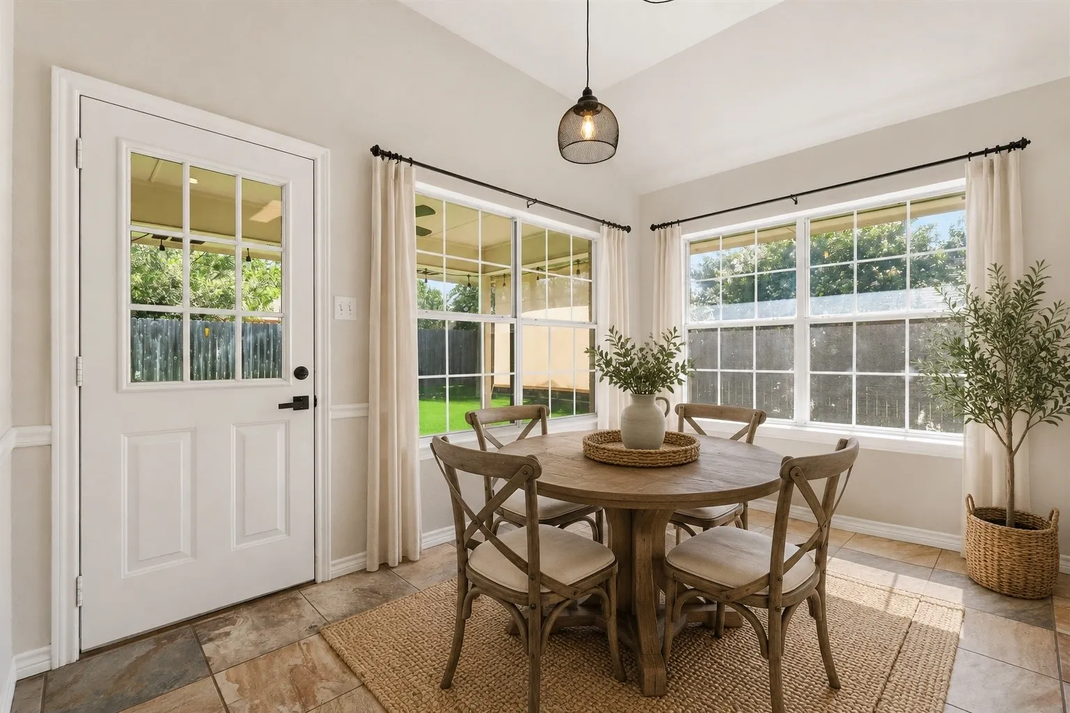 Dining area featuring multiple windows, a glass-paneled exterior door, tile flooring, wainscoting, and a contemporary pendant light fixture