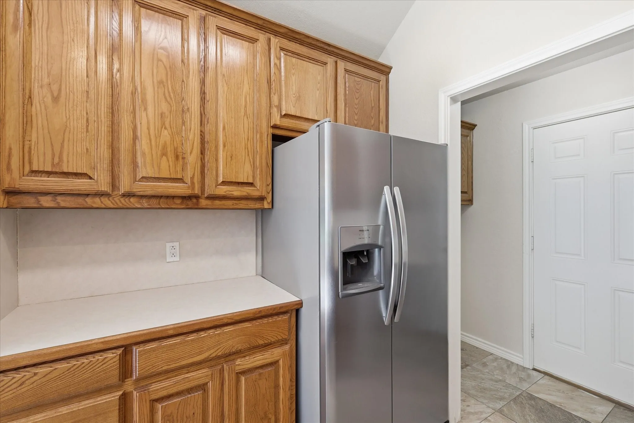 Wood-finish cabinetry with panel doors and a light-toned countertop, complemented by a stainless steel side-by-side refrigerator