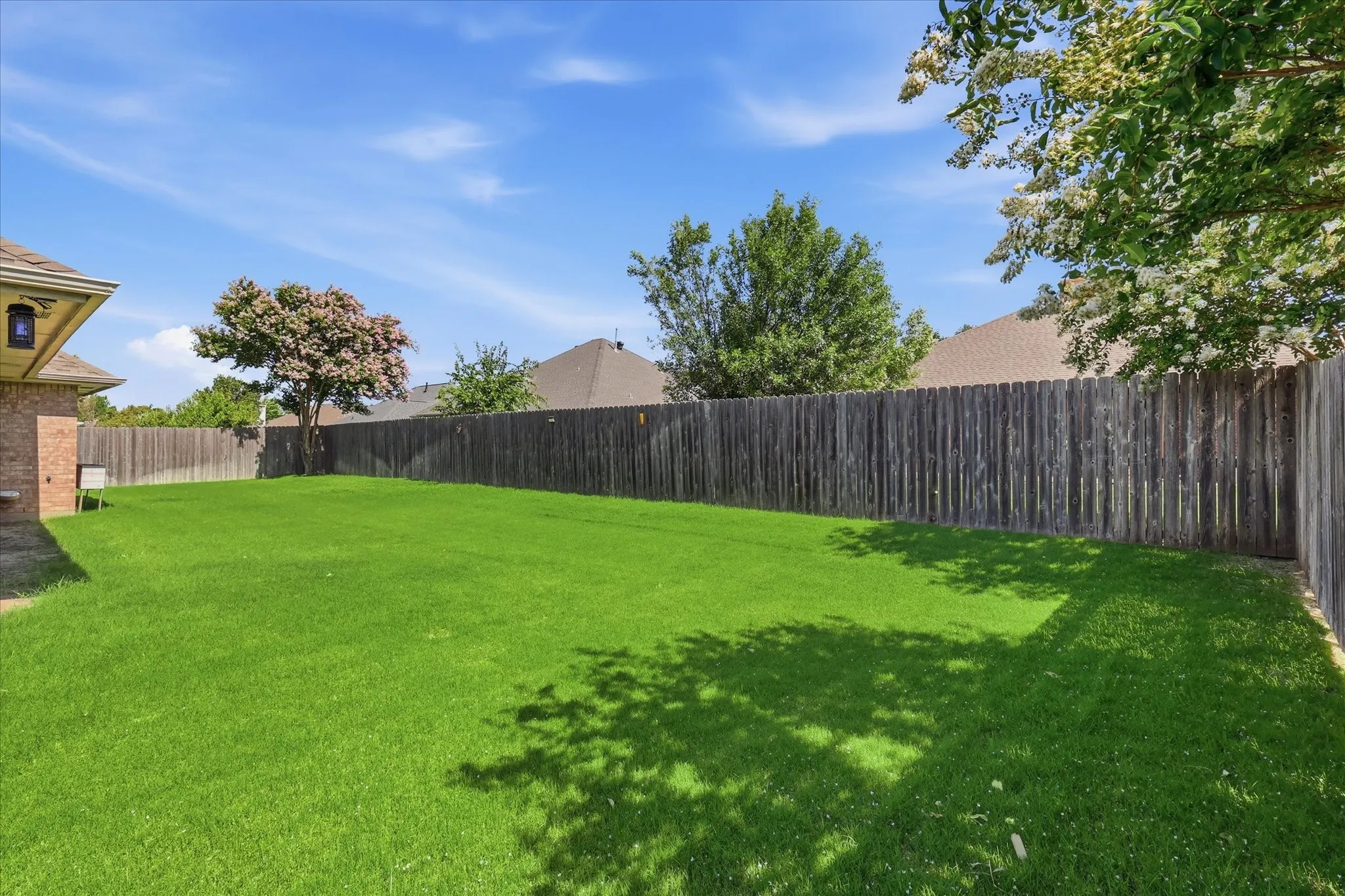 Spacious backyard featuring a lush green lawn, full wood privacy fencing, and mature trees