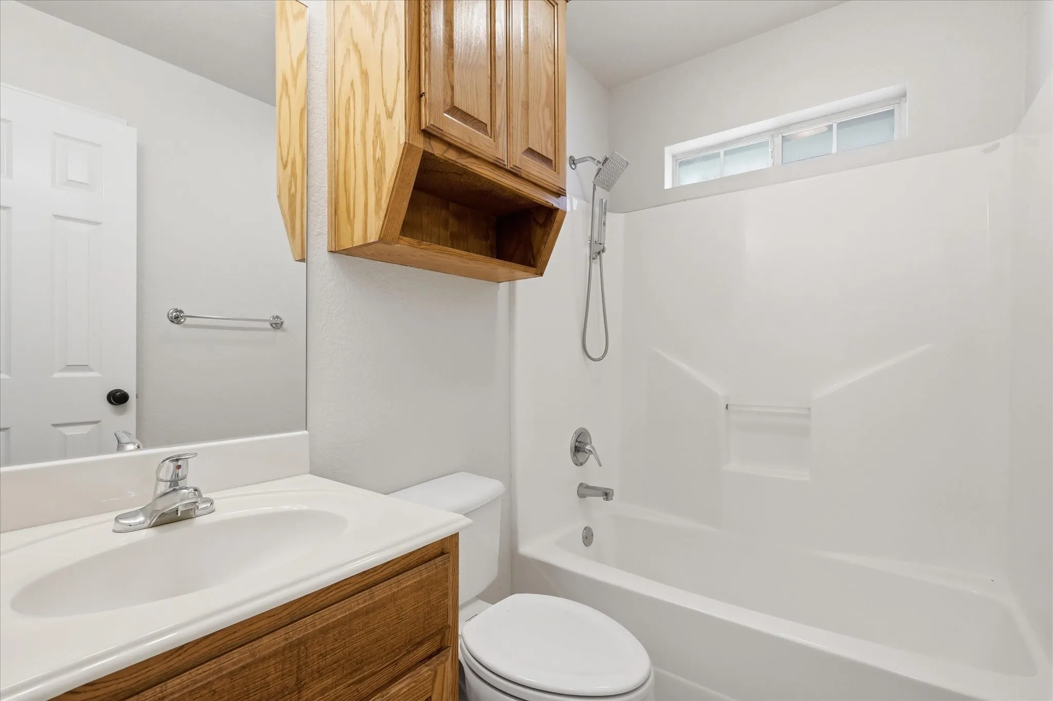 Bathroom featuring a white bathtub and shower combination, a transom window, a single vanity with a white countertop and integrated sink, a chrome faucet, and wood cabinetry