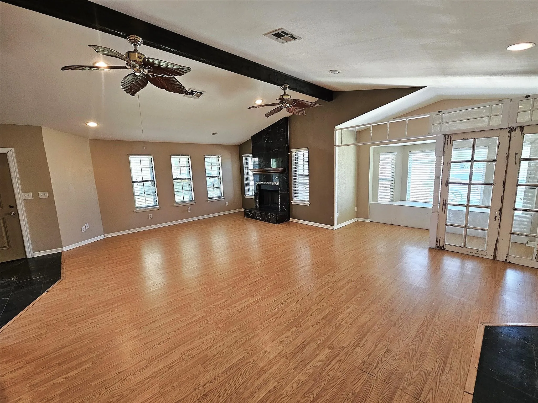 Spacious living area featuring wood-finish flooring, a vaulted ceiling with exposed beams, and multiple ceiling fans