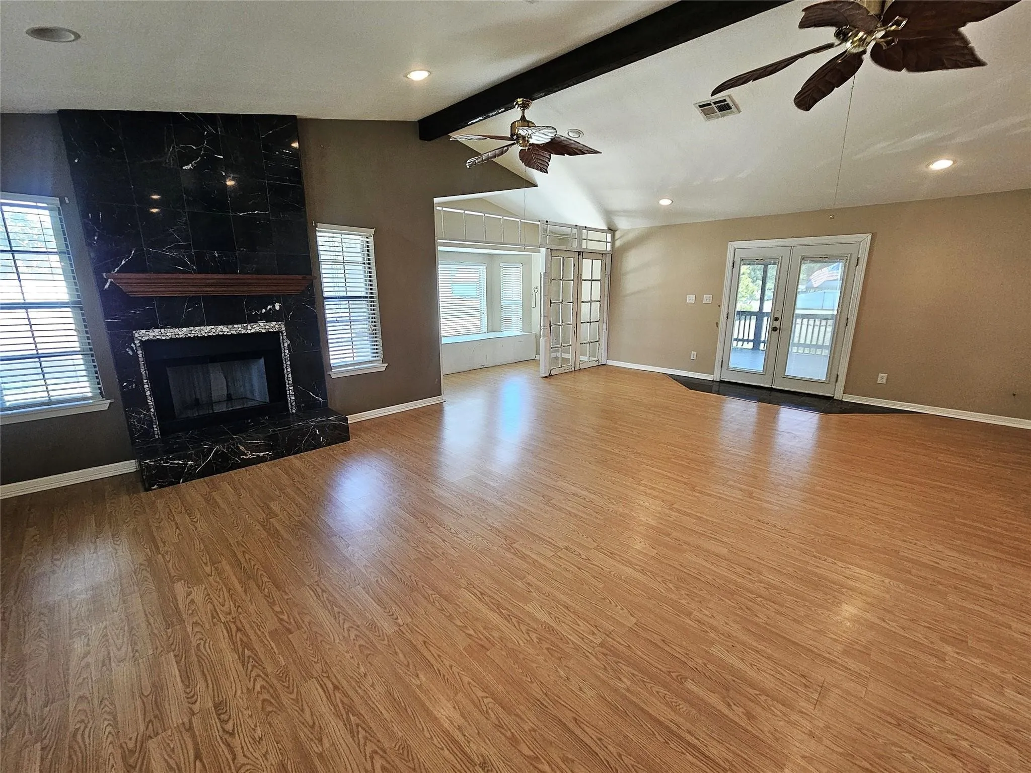 Spacious living area featuring wood-finish flooring, a black marble-look fireplace with a wood mantle, vaulted ceilings, and recessed lighting