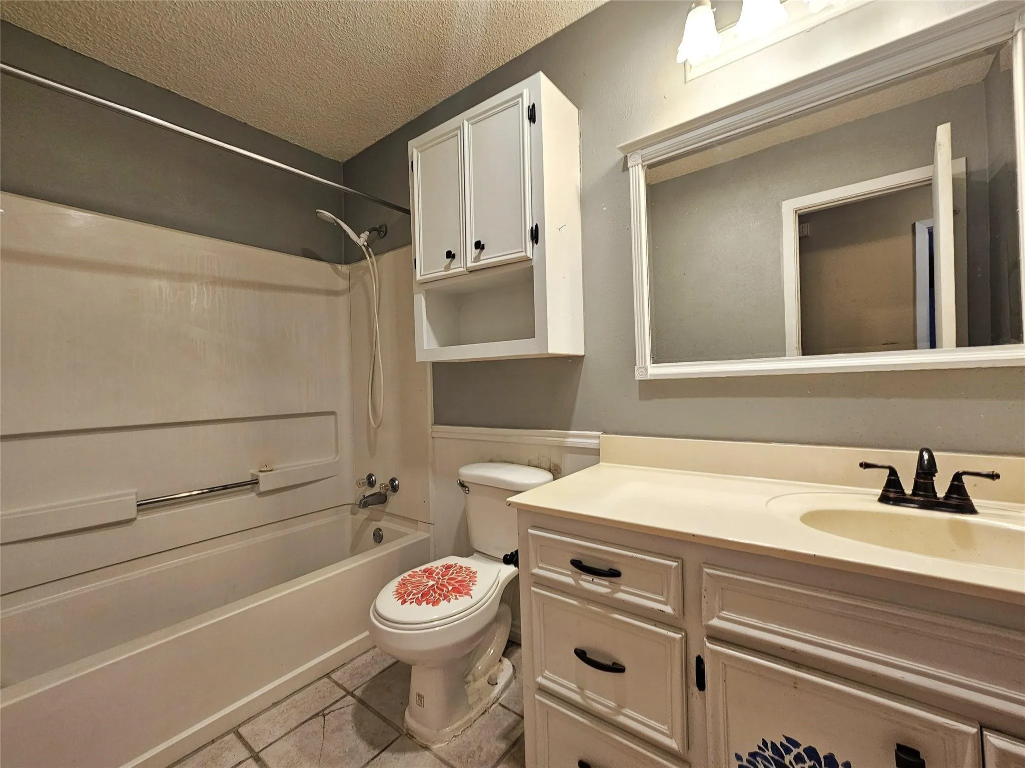 Bathroom featuring a full tub and shower combination, a single vanity with an integrated sink, a framed wall-mounted mirror, overhead lighting, and built-in wall cabinetry