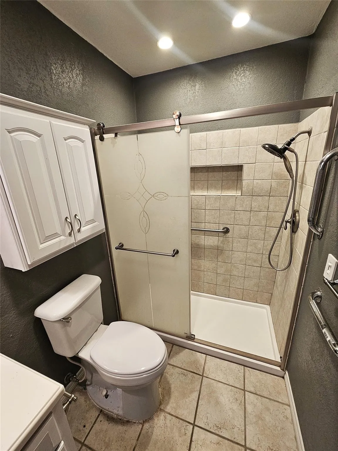Bathroom featuring a tiled shower with sliding frosted glass doors, integrated shower niche, and grab bars