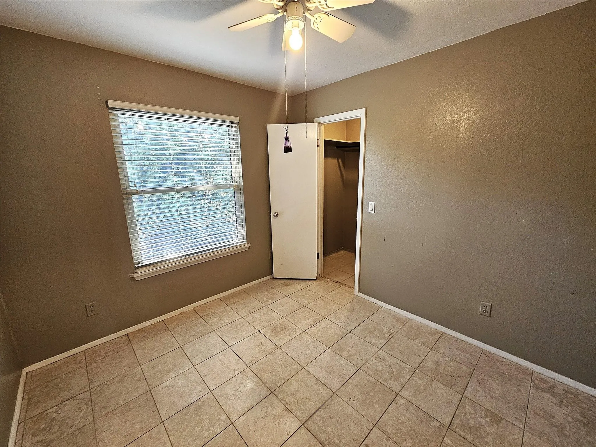 Room featuring light-toned tile flooring, textured neutral-toned walls, and a window with horizontal blinds