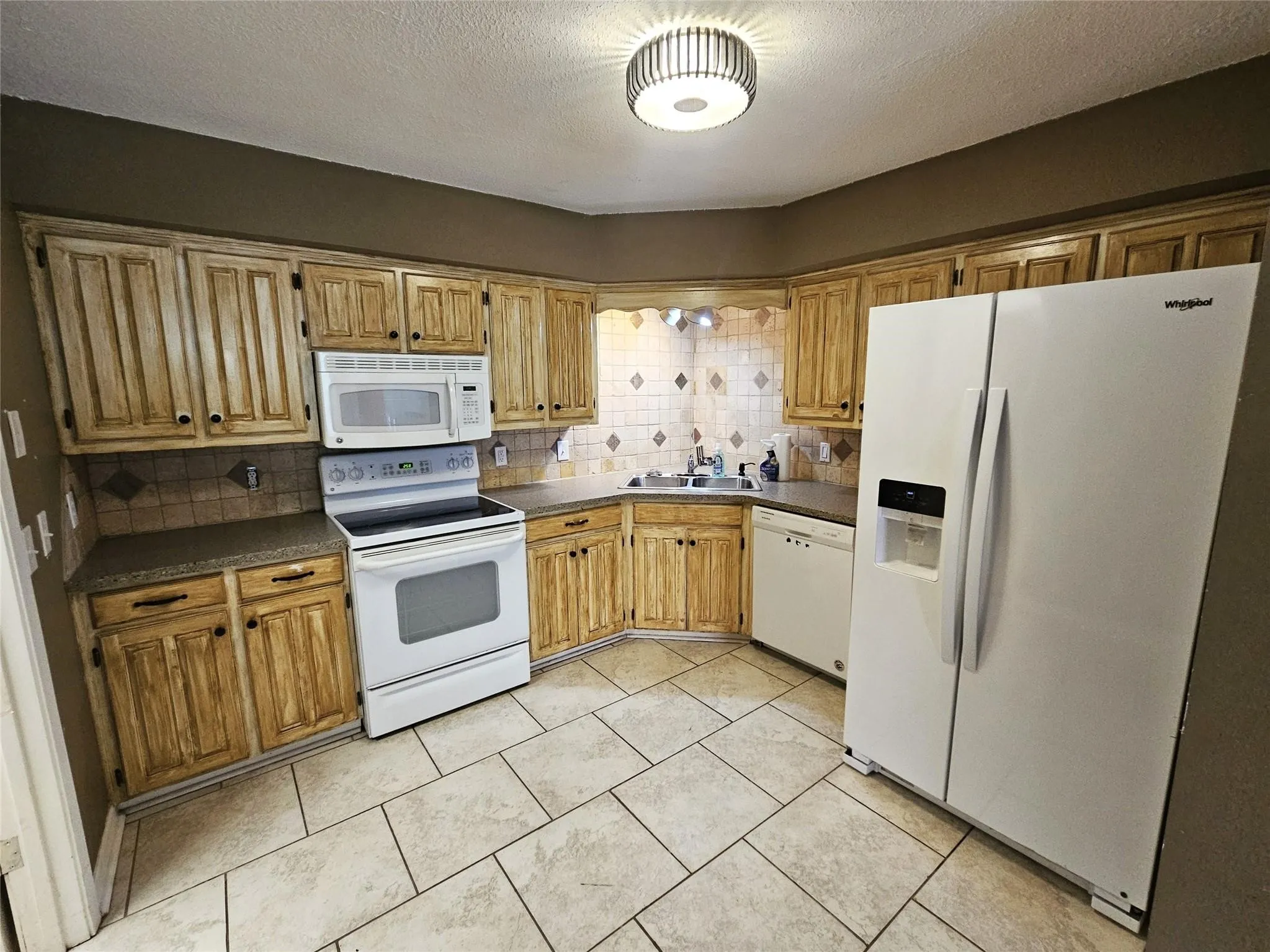 Corner kitchen featuring wood-finish cabinetry, a tile backsplash, and a large side-by-side refrigerator