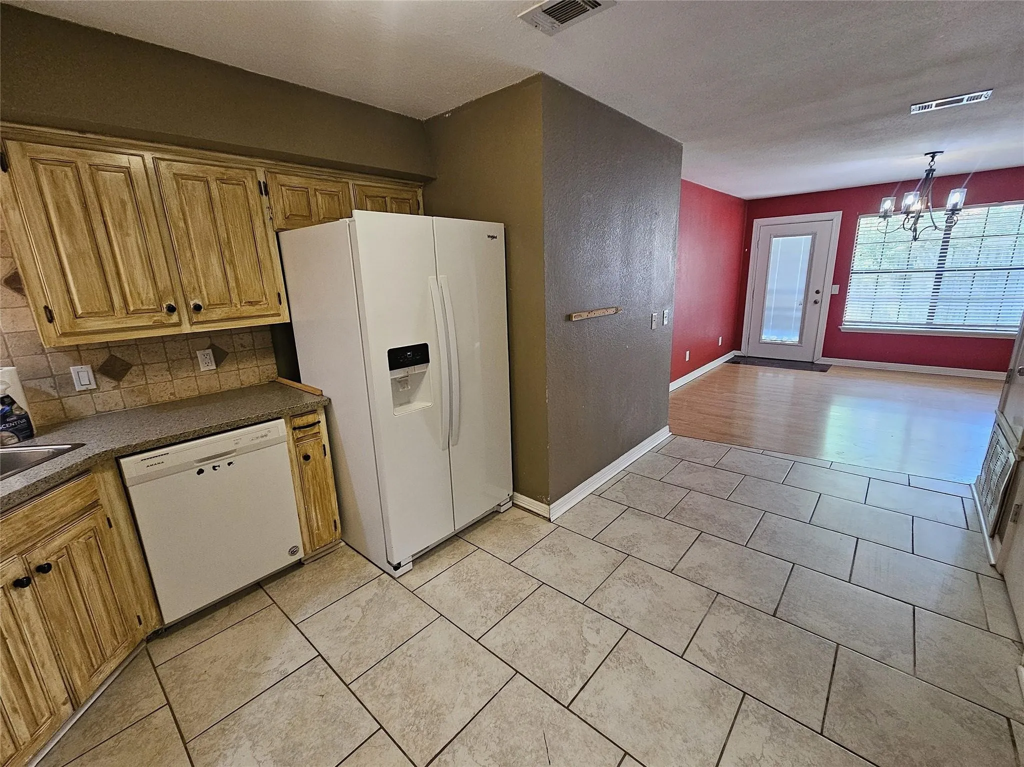 Kitchen featuring wood-finish cabinetry, tile backsplash with decorative accents, and a built-in dishwasher