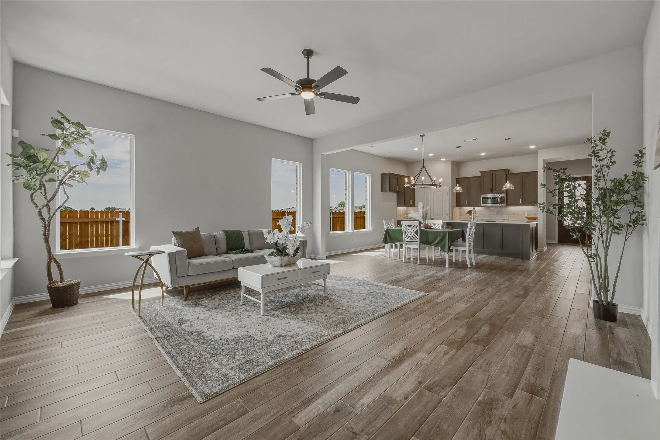 Open-concept living space featuring wood-finish flooring, a contemporary ceiling fan, recessed lighting, and a kitchen with an island and pendant lights